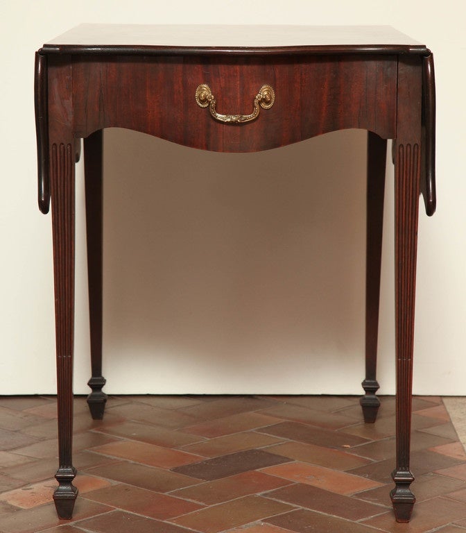 A fine and unusual George III mahogany serpentine front pembroke table with butterfly leaves, the figured top with barber-pole banded edge over an apron fitted a drawer opposing a mock drawer and on stop-fluted legs ending in turned and tapered