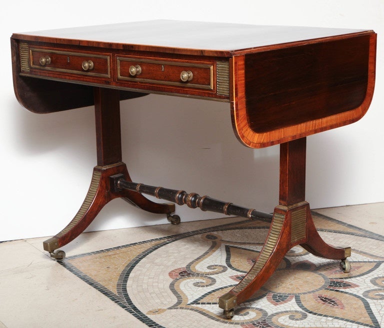 A Regency rosewood and satinwood cross-banded sofa table with turned stretcher base and brass mounts in the manner of John McLean.