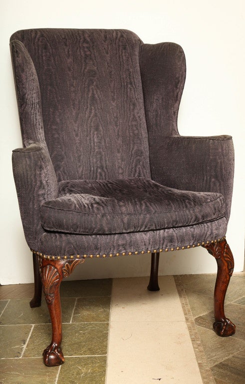 A George III upholstered walnut wing chair with outscrolled arms with shell carved knees and claw and ball feet.