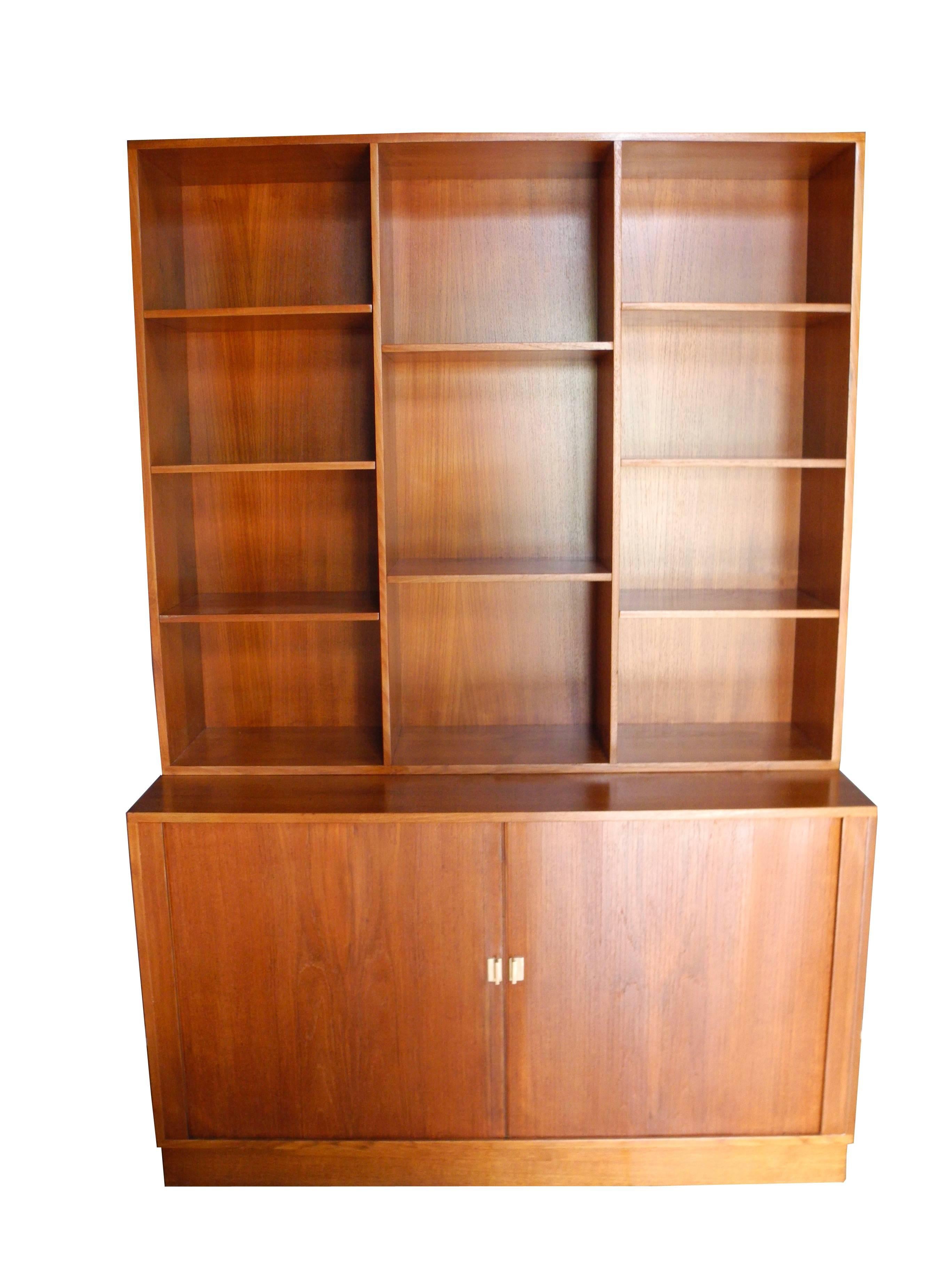 This unique and handsome Danish Modern bookshelf and lower cabinet consists of two tambour doors that wrap around the back of the cabinet when opened. The tambour door pulls are made of solid brass. Up top simply sits a teak bookshelf or display