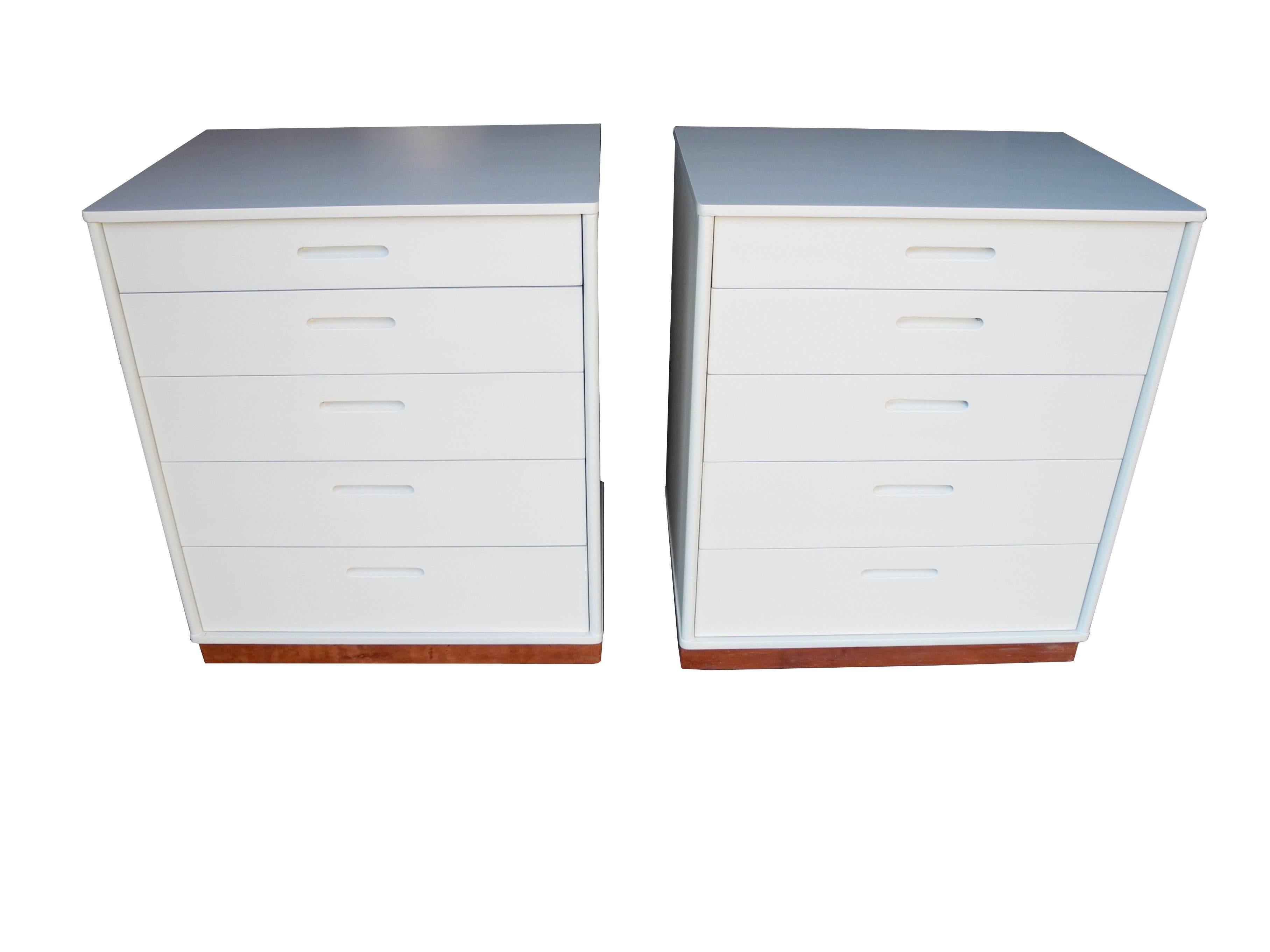 These small white matching dressers or nightstands equipped with five drawers each are painted in a linen white and lacquered. The plinth is wrapped in leather and the rounded side edges are examples of Wormely's attention to detail.