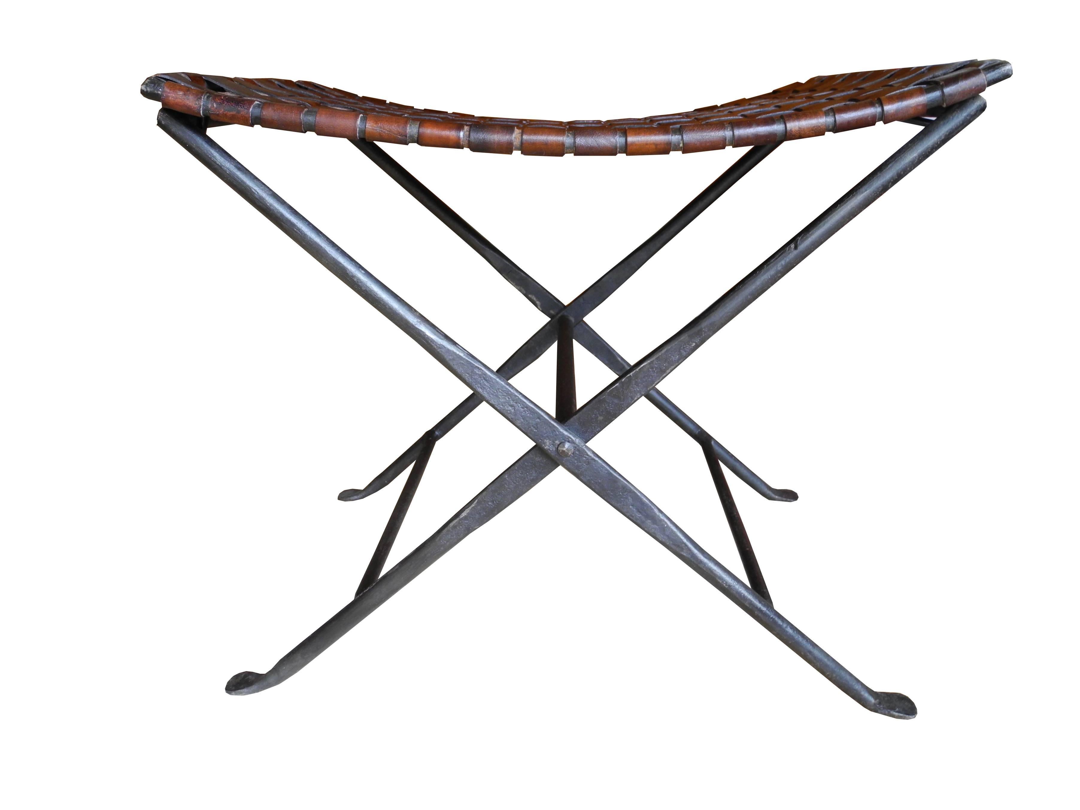 This folding stool has been handcrafted. Made of forged wrought iron and brown strips of woven saddle leather. Beautifully made.