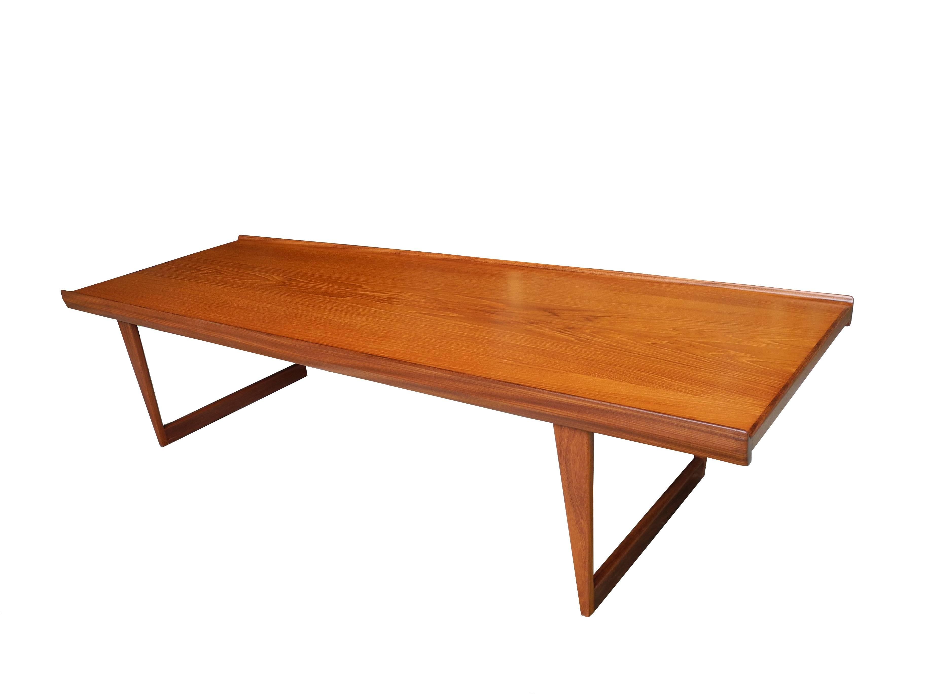This beautifully crafted Danish Modern teak coffee table has tapered framed legs and a lip on each long edge. Designed by Løvig Nielsen in the 1960s.