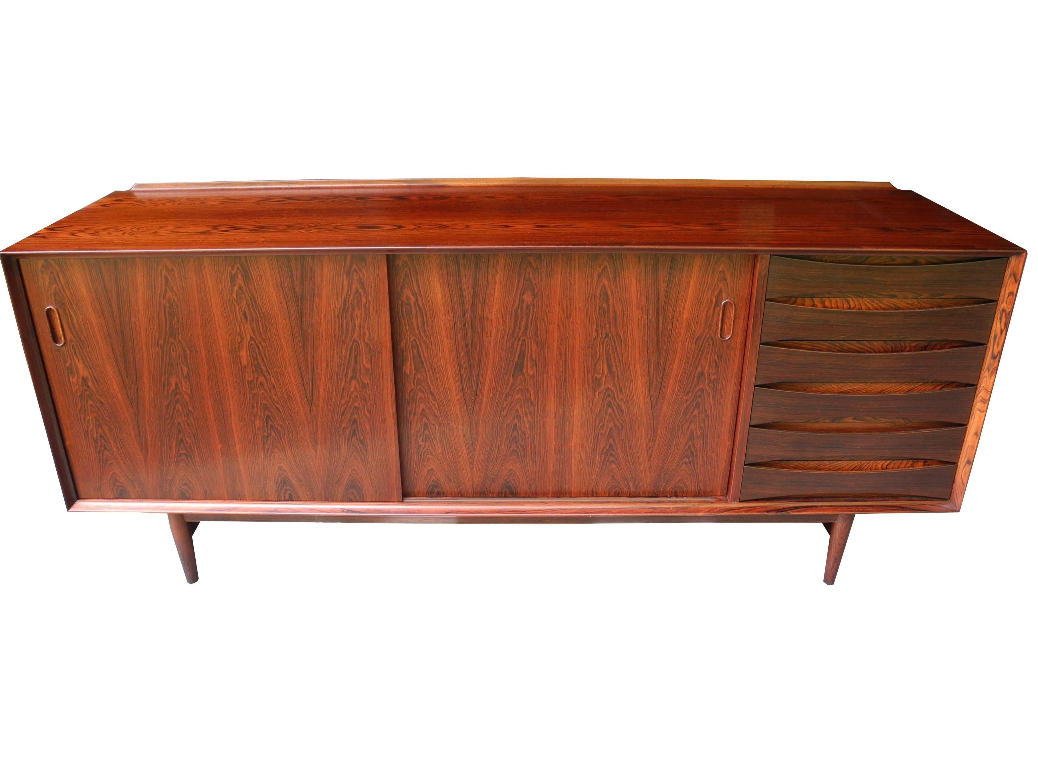 This Danish modern sideboard designed by Arne Vodder and made in Denmark is a rare find in rosewood. This credenza has six drawers on the right and a two-door cabinet with adjustable shelves on the left. The top has a practical designed back lip.