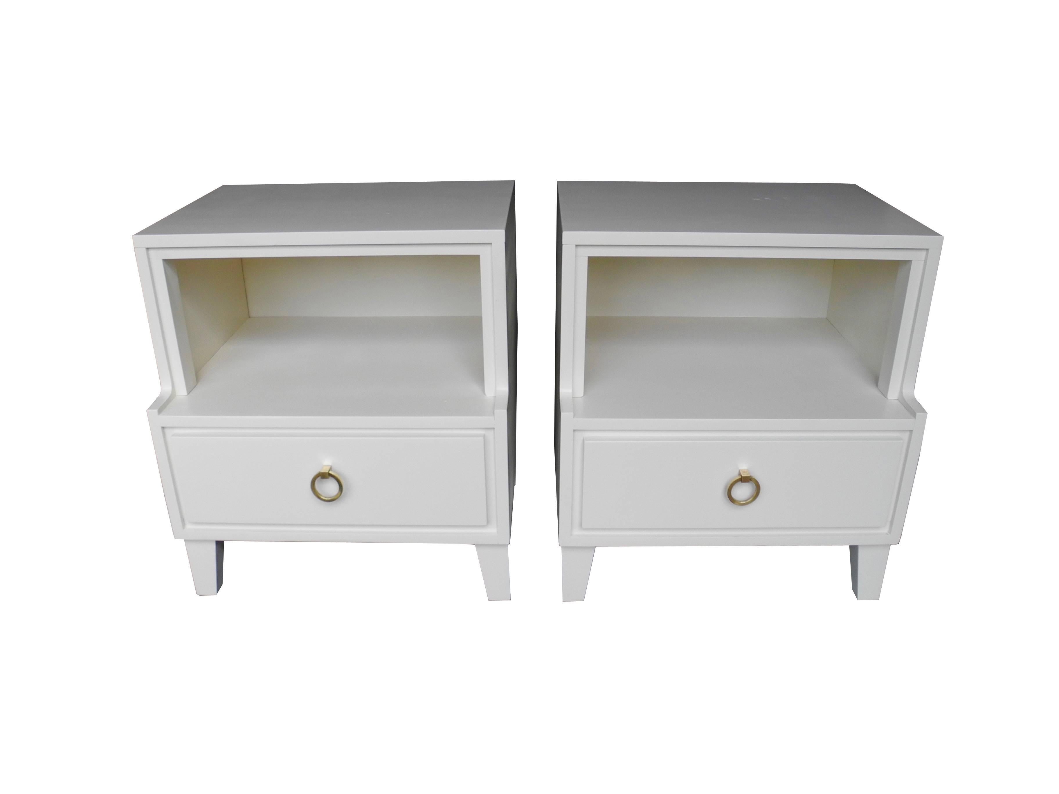 These nightstands or bedside tables are painted linen white or off-white. They have a cubby shelf and a drawer with a solid brass pull. Modern lines, plenty of storage, vintage, by Conant Ball, 1950s. The tops are 15.5