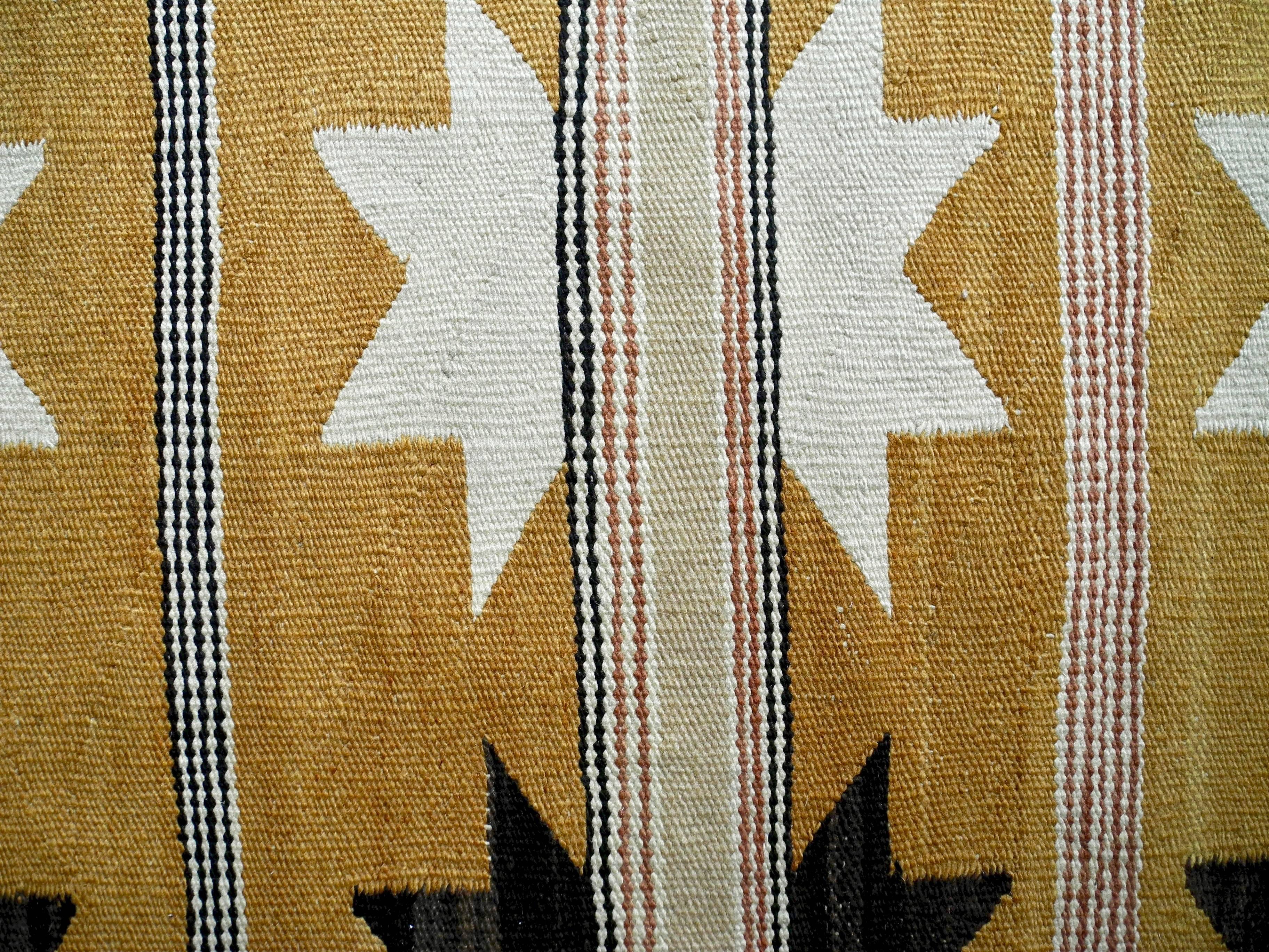 This Navajo rug is a simple / minimal design of eight point stars in black and white, on an ocher yellow background with intersecting stripes in natural wool tones.