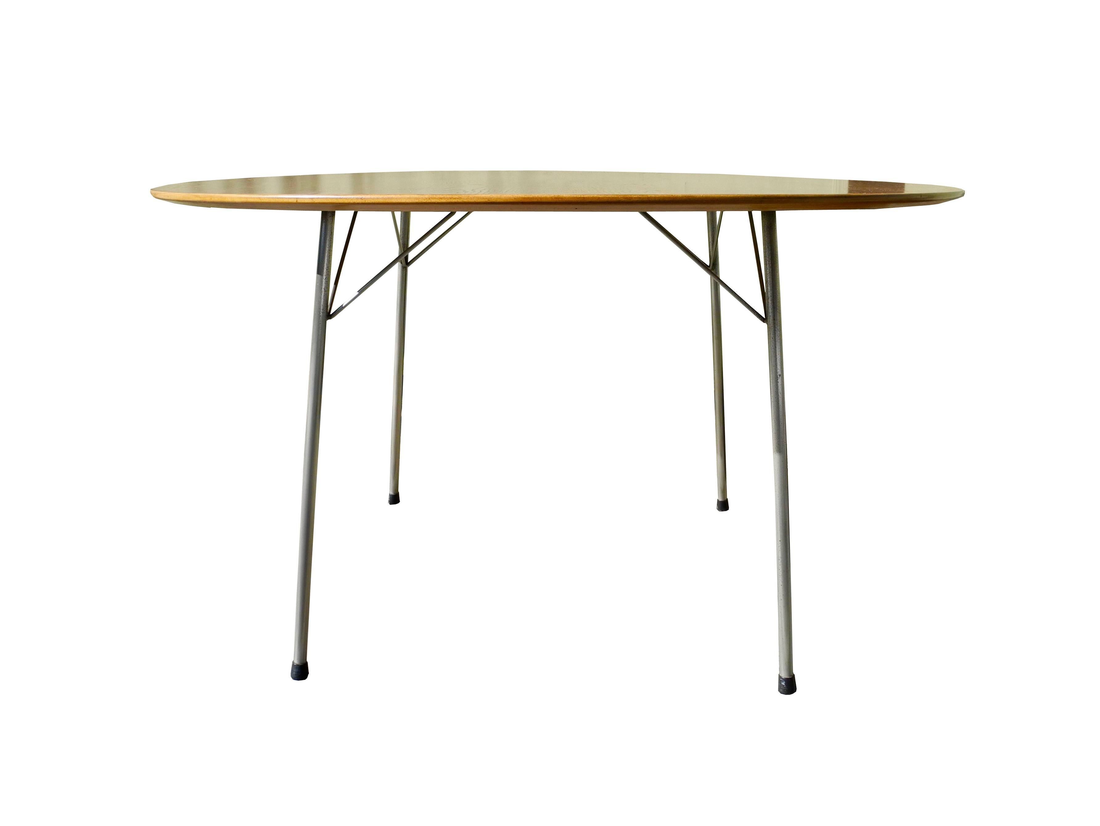 This round table has a bevelled oak top with plated steel legs. It was designed by Arne Jacobsen.