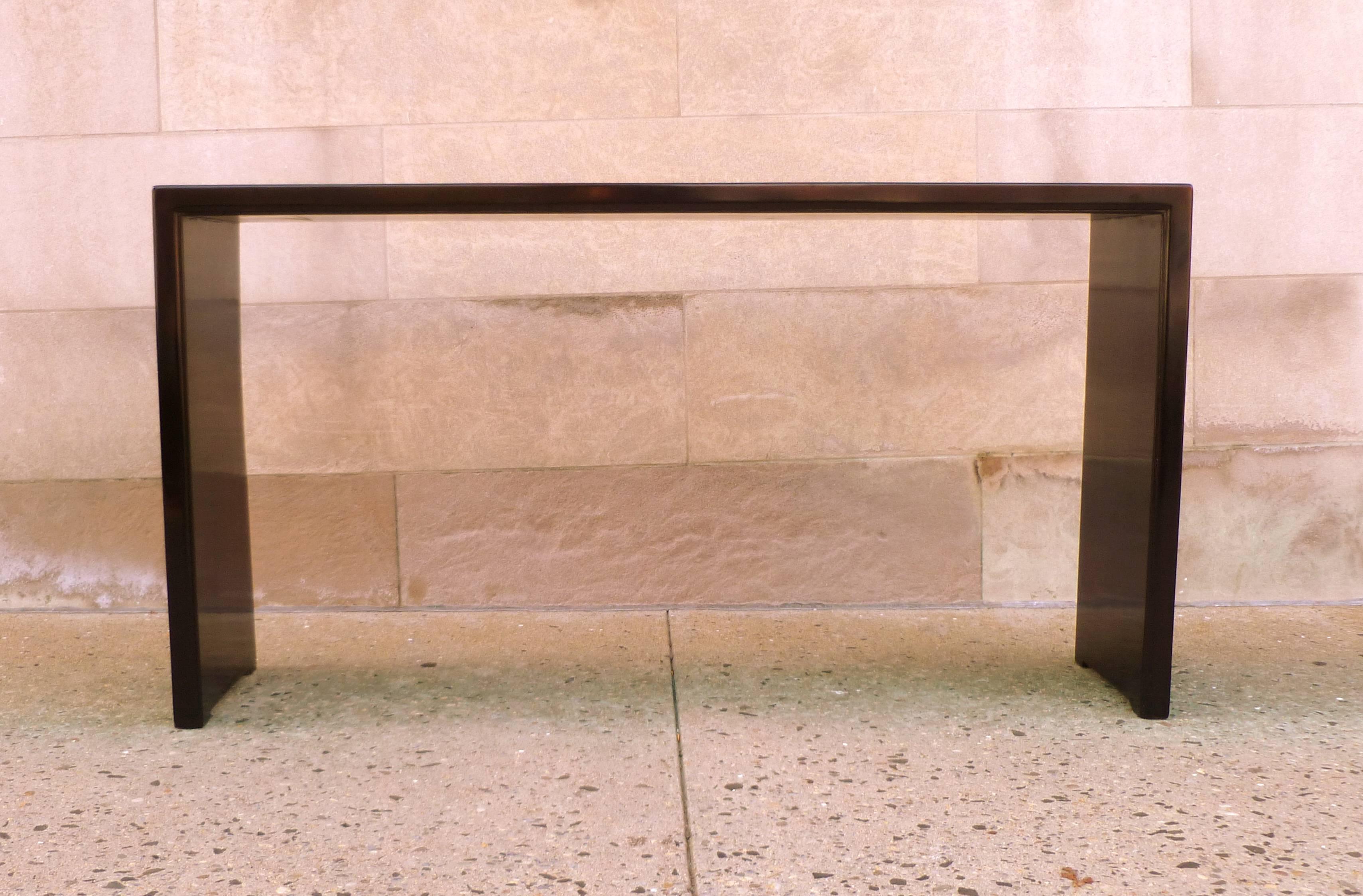 A simple and refined black lacquer console table, single plank top supported by waterfall legs.