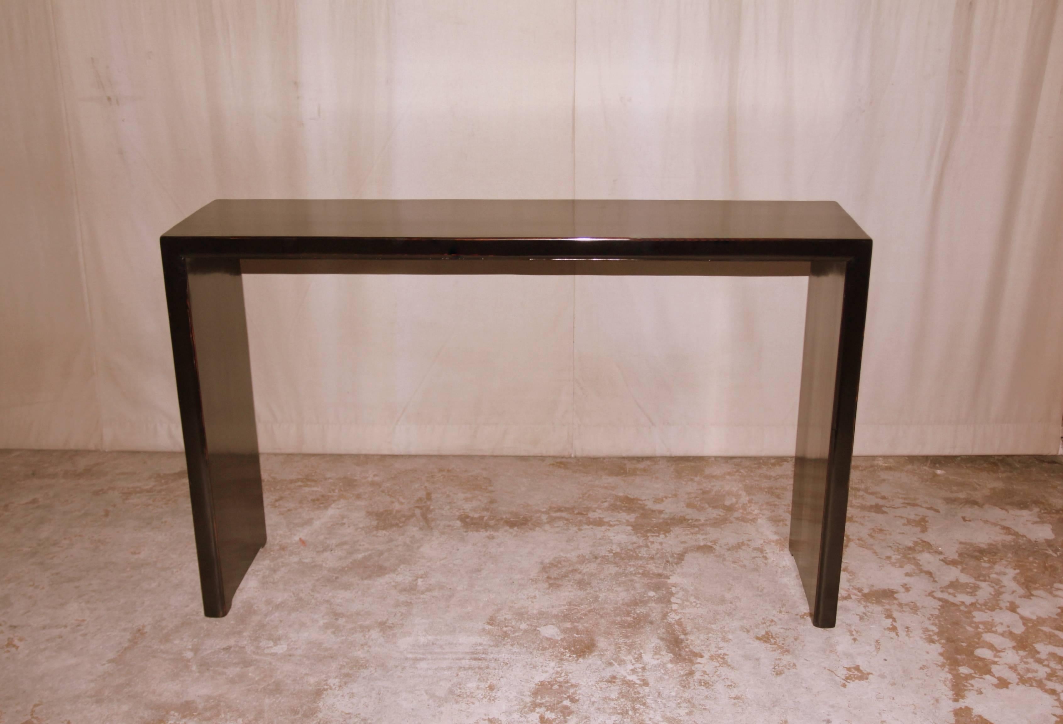 A simple and refined black lacquer console table, single plank top supported by waterfall legs. Pair available. Beautiful color, form and lines.