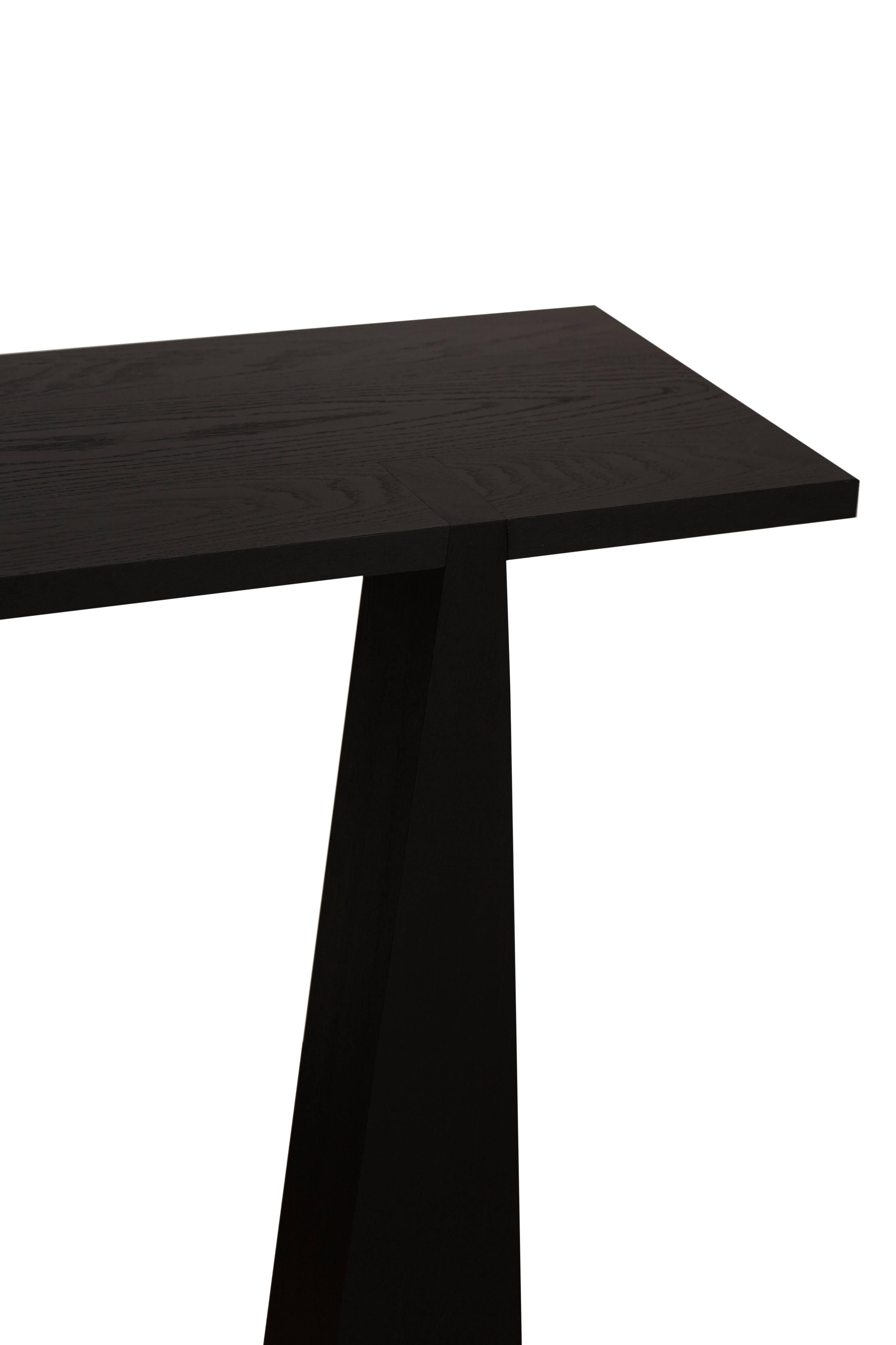 Nylander solid oak tapered three-leg console table shown in a matte black open grain finish. Solid construction and exposed joinery on top detail this sculptural form.