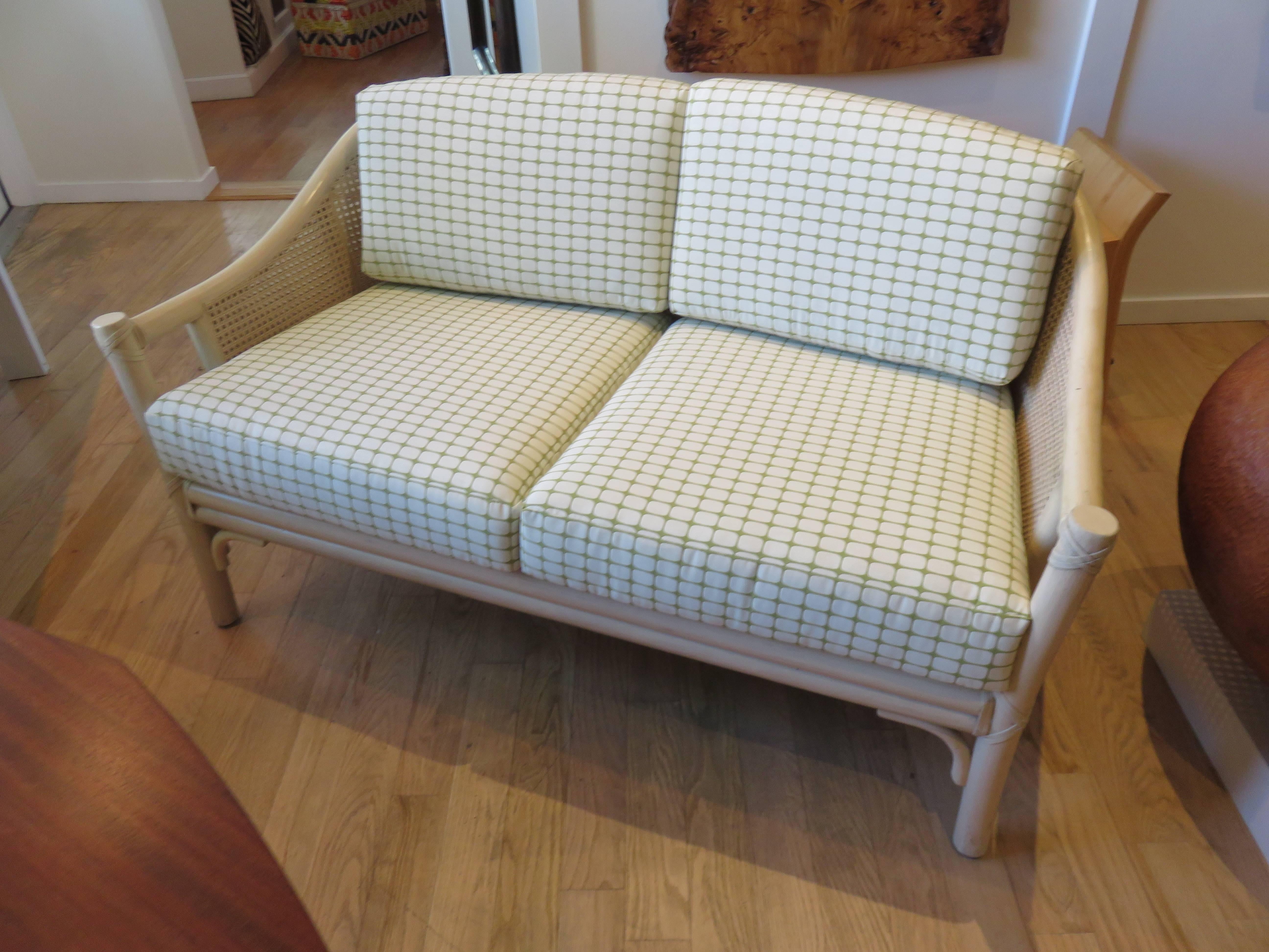 A two-seat bamboo and cane McGuire settee from the 1960s.
New upholstery in a a retro style Kravet fabric. Four apple green and beige 
dacron and foam filled cushions. The frame and cane stone beige finish is original.
There are two matching