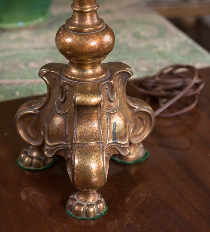 Sophisticated gilded metal table lamp with burnished overlay. Slender shaft with carved three footed base in Baroque style supporting two-light sockets with separate chain pulls. Topped by off-white silk octagon shaped shade with brass finial. Shade