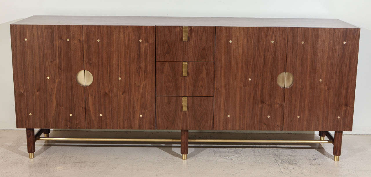 The Niguel cabinet features three central drawers. On the left is a single compartment with one adjustable shelf. On the right, are two compartments, each with an adjustable shelf and one with a drawer. Details include leveling brass cap feet, a