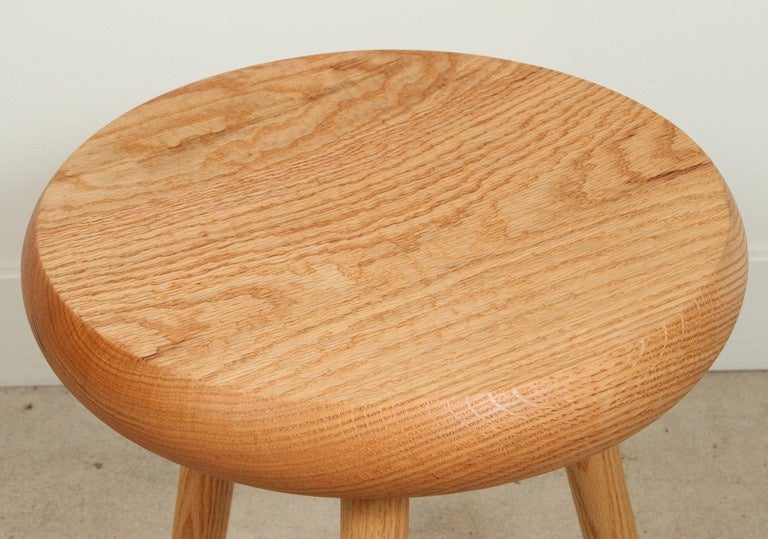 The Dibbet stool by De JONG & Co. is made from solid oak and features a carved seat with three doweled legs.