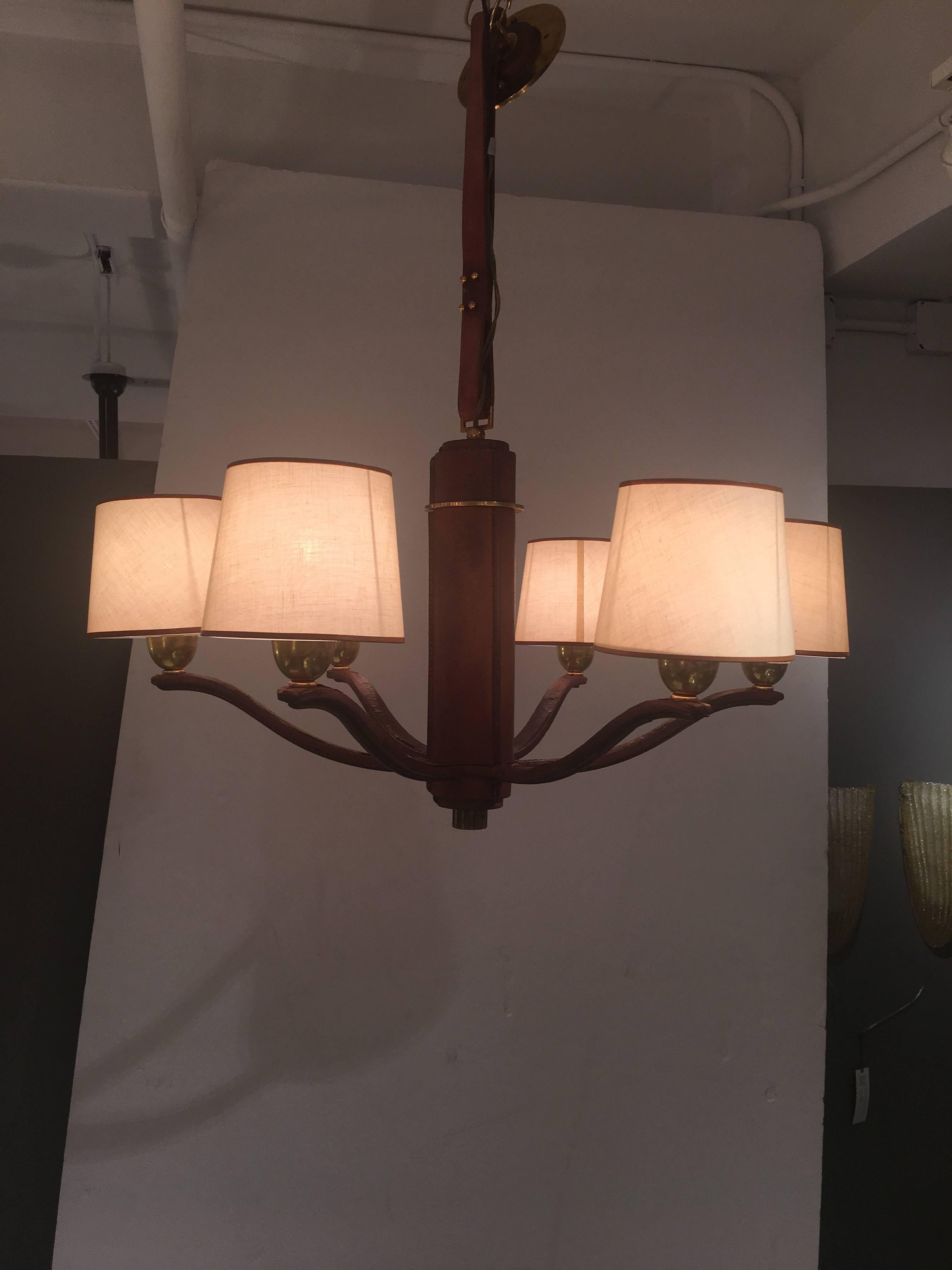 Six-arm chandelier in brown pigskin and polished brass. By Longchamp, Paris, 1960s. Retains original linen shades and glass diffusers and ceiling mount. Great overall age patina to leather, there is a little dryness and cracking on tops of arms