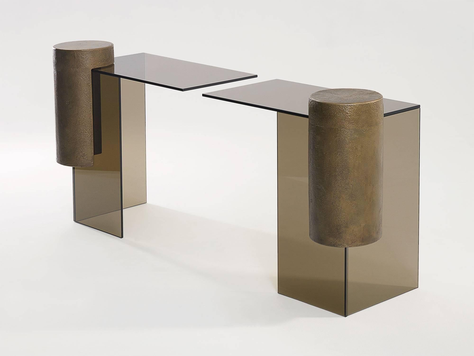 Smoked glass and brass console table comprised of two separate tables reaching towards each other by Los Angeles designer Brian Thoreen. Cantilevered by a brass column, the glass elements reach towards each other to create the table surface.