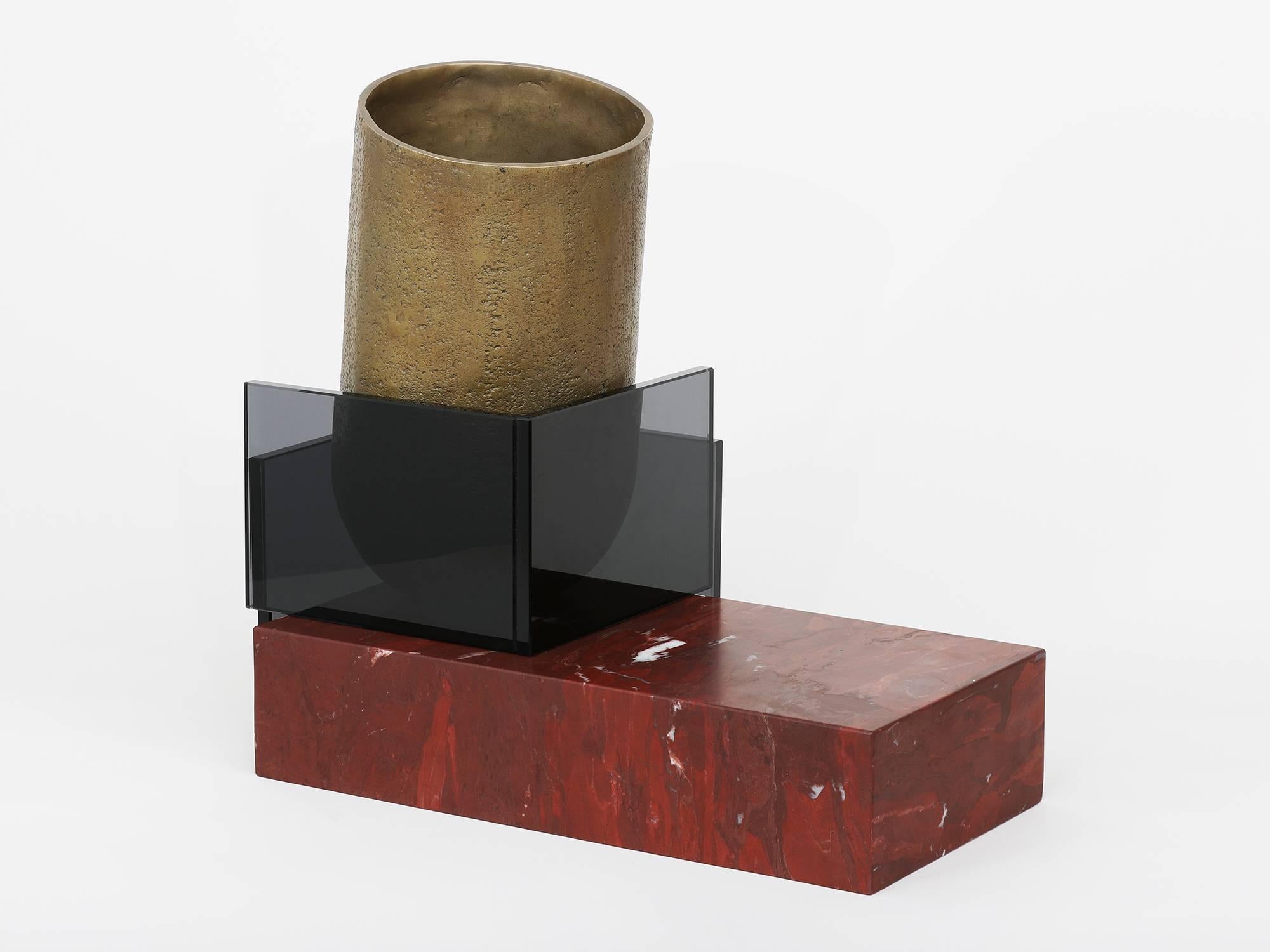 L'un des trois vaisseaux développés comme maquettes de matériaux pour les œuvres plus grandes de Brian Thoreen. Composé d'un récipient en bronze moulé, de marbre rouge et de verre gris. Disponible également en marbre brun ou gris et en verre bronze.