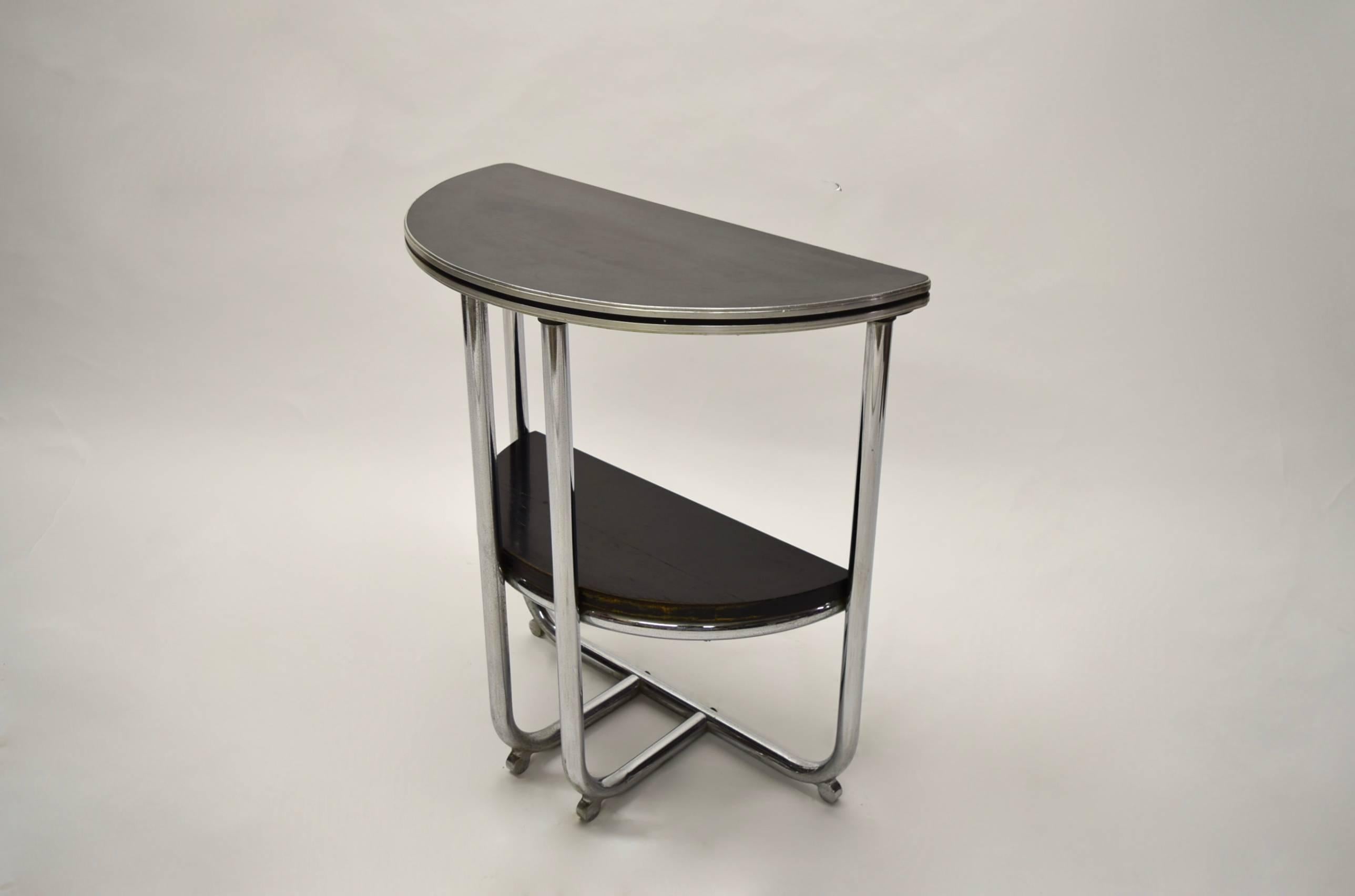 Demilune American Art Deco console table in tubular chromed metal, a black lacquered wood shelf, a black laminate top, and four round chromed feet.