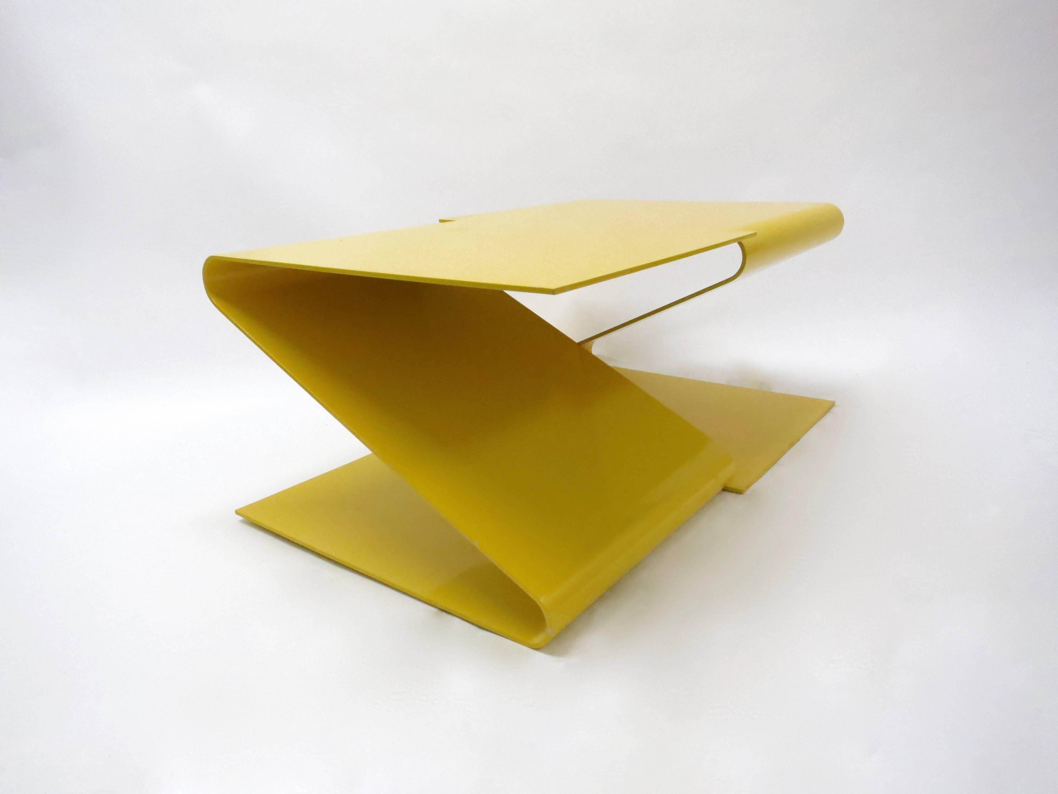 La table à café ou à cocktail géométrique conçue par L.E.FT Architects se compose d'une seule pièce d'acier émaillé jaune, coupée et pliée, comportant deux segments en forme de Z qui se reflètent, avec des courbes arrondies et des angles droits sur