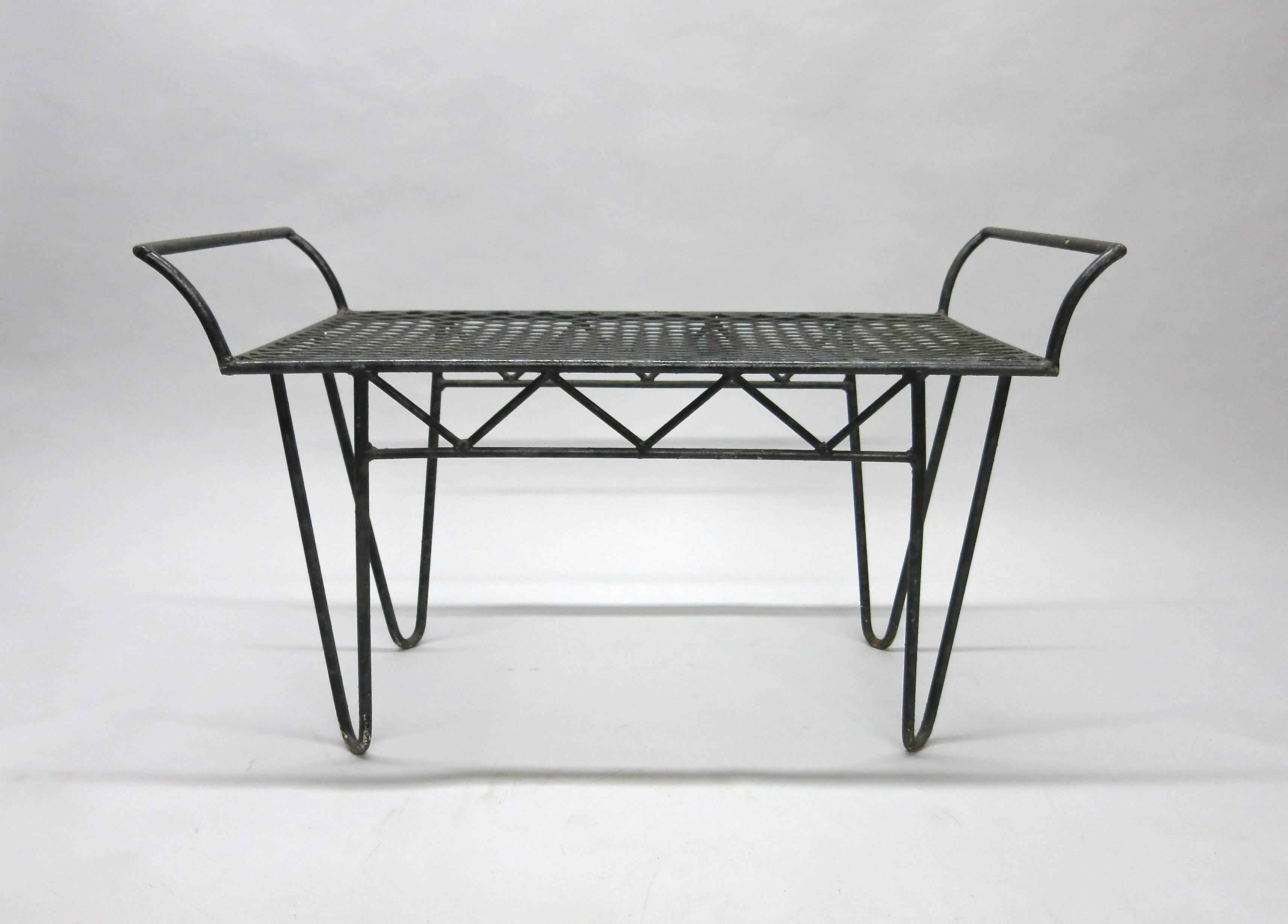 Wrought iron bench with four hairpin legs and a mesh metal seat with arched arms on each side and inverted 