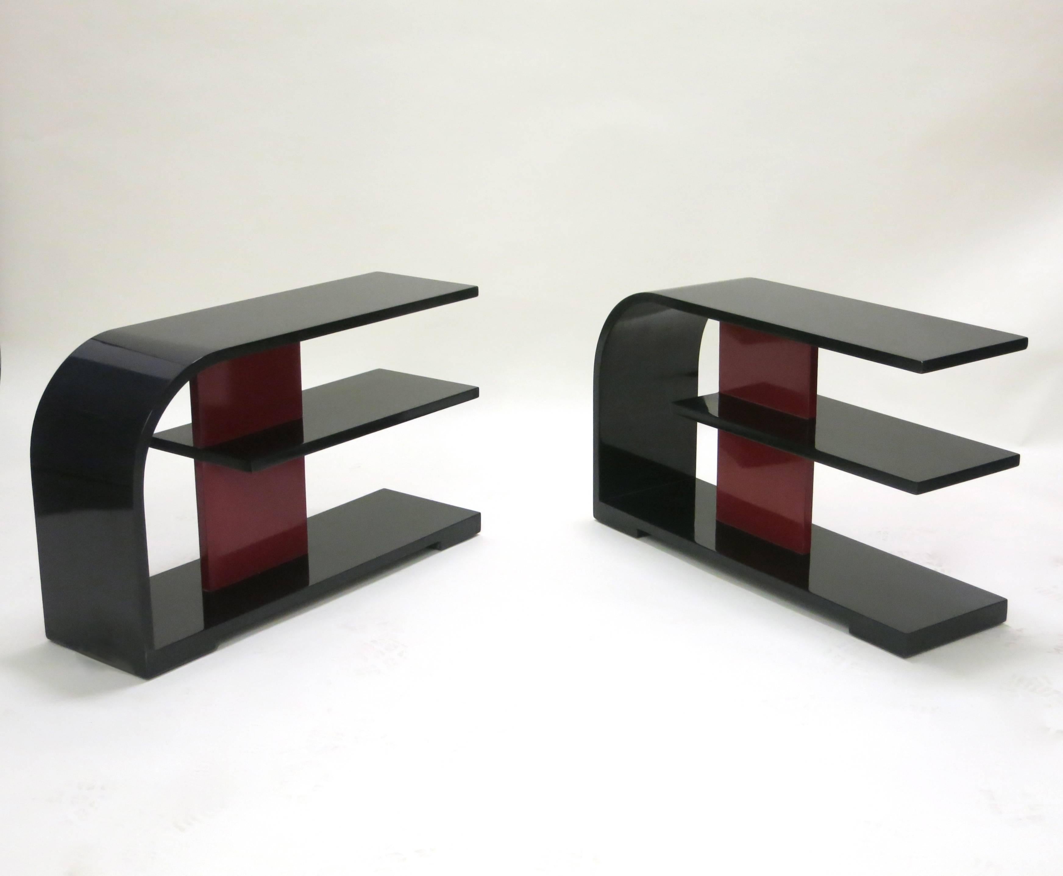 Pair of tri-level side tables refinished in black lacquer and red lacquer detail. The top shelf bends to form the back connecting to the lower shelf that acts as the base having a support at each corner.