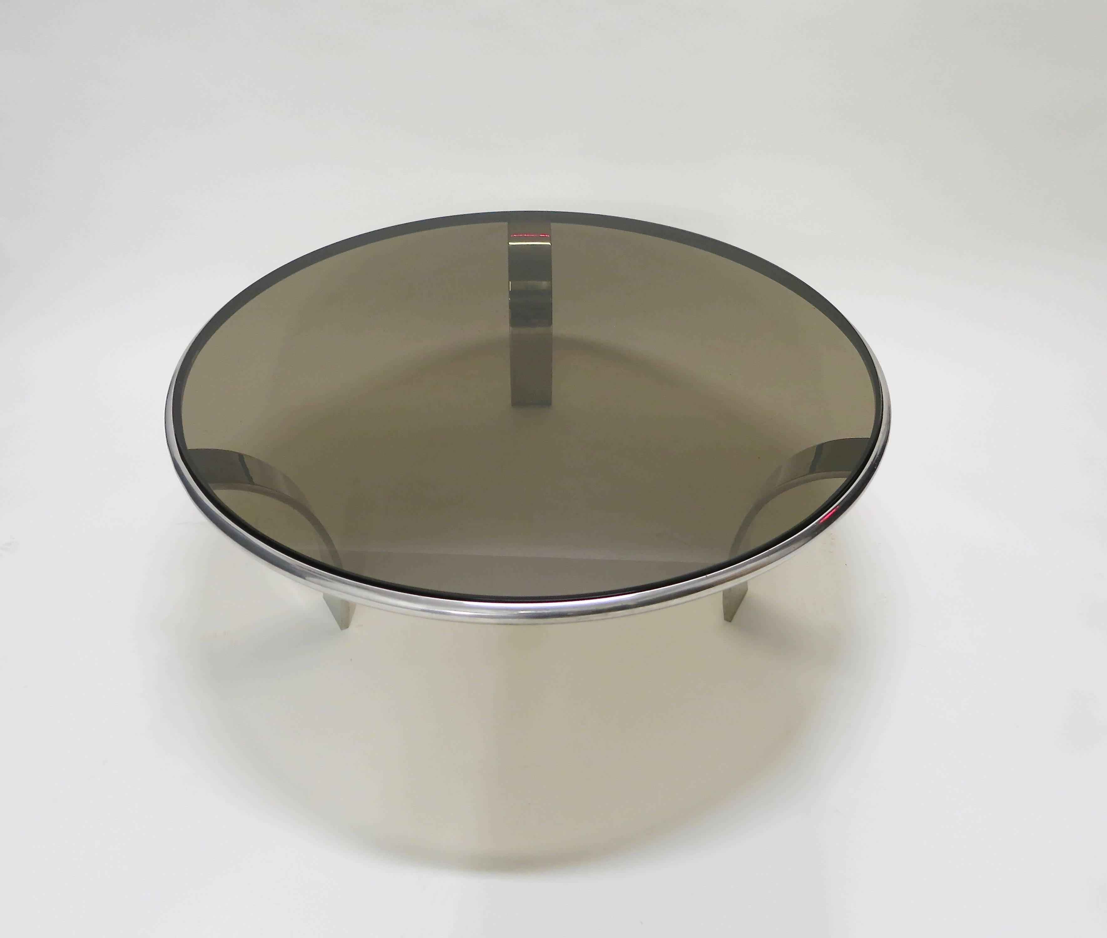 Coffee table has three arched legs. Each leg is a 1/2 inch solid, polished, steel and holds the round frame all supporting a inset smoked glass top that is 42 inches in diameter and 1/2 inch thick. Great vintage condition.