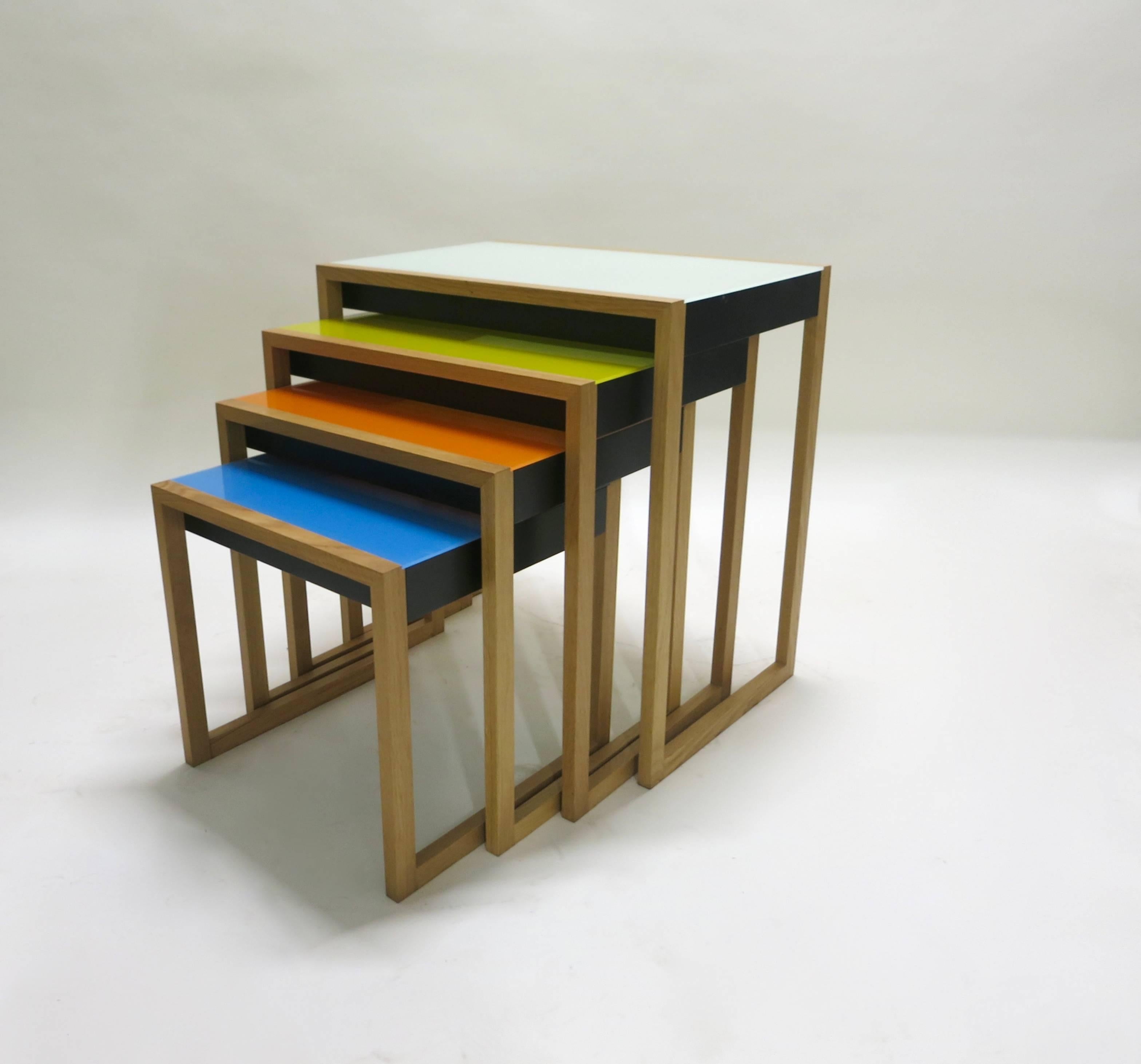 Set of four, sled-based nesting tables in oak and colored acrylic glass, originally designed in 1926 by Josef Albers and reissued by Vitra from their 2004 production, and each labeled. Colors in descending order from size: pale aqua, yellow, orange,