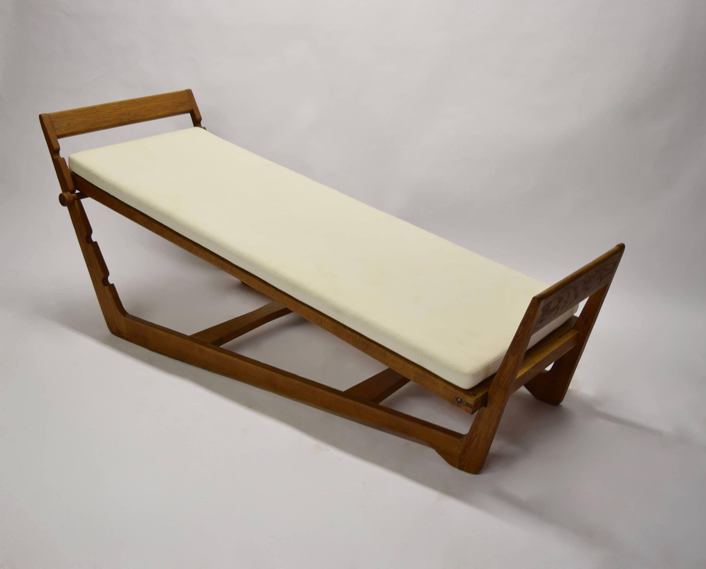 Solid oak daybed with a muslin seat cushion. The frame has four sets of, hand carved, notches. Each set of notches determines the incline of the cushion. The fifth setting is achieved by resting the cushion flat into the frame, having no incline. A