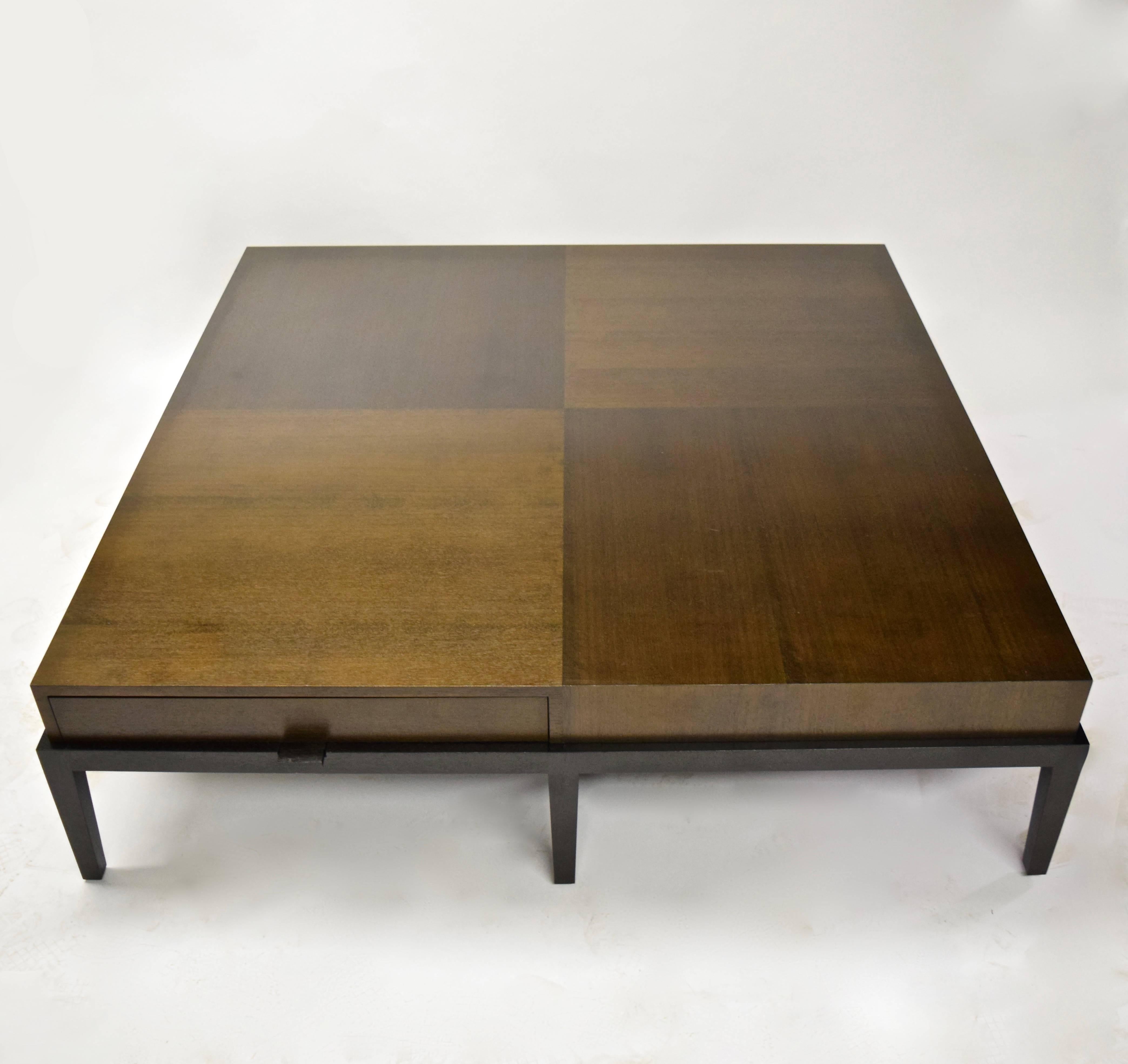 Large coffee table has a square walnut top divided into four sections each with opposite wood grain for a checkered visual detail. The 58 1/2 inch top has two drawers each with solid patinated bronze pulls, all resting on a solid wood base with