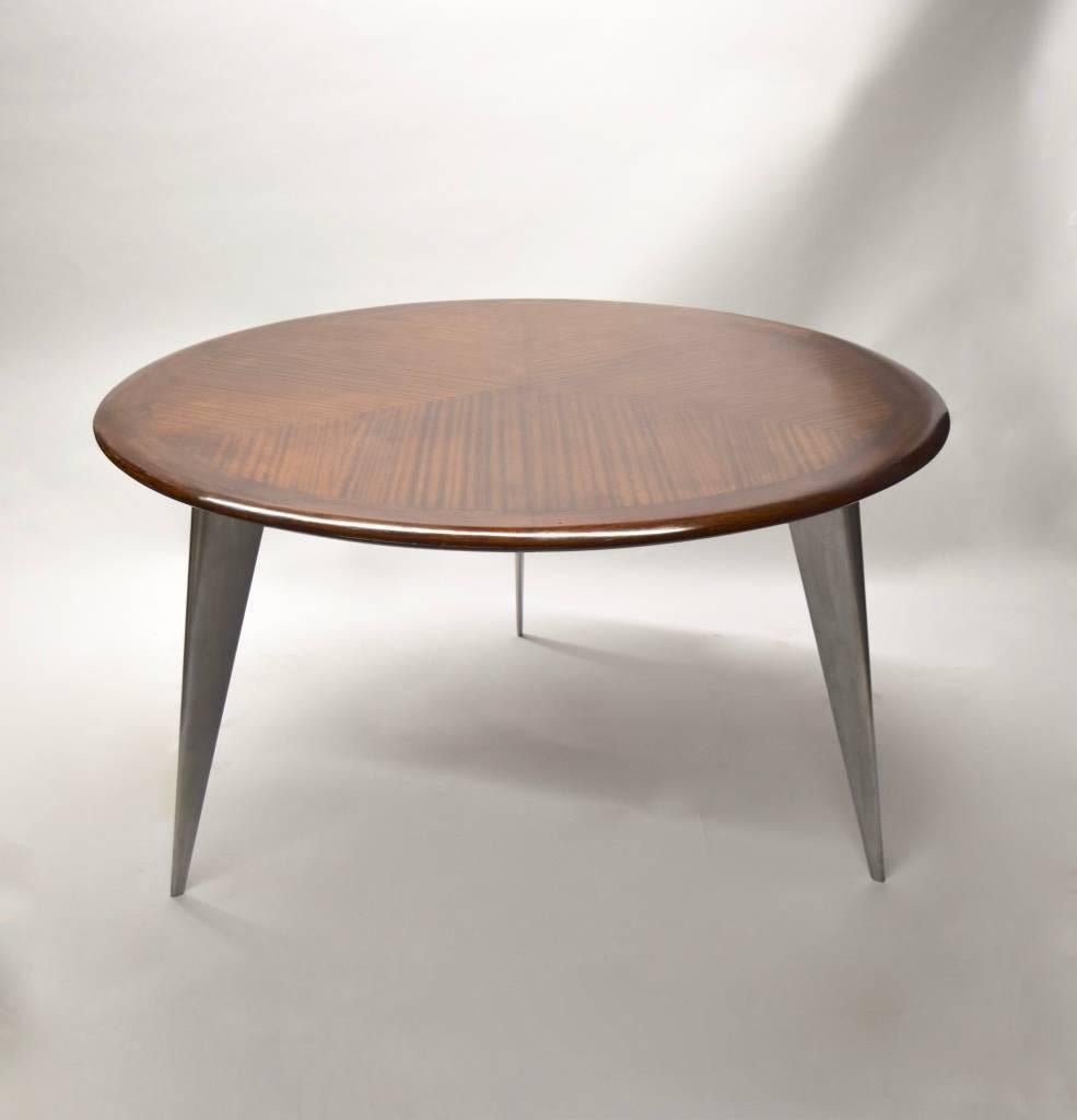 Dining table with a thick, round wood top that has six matchbook veneered sections and a Fine rounded edge, supported by three angled legs in polished aluminum, each signed 