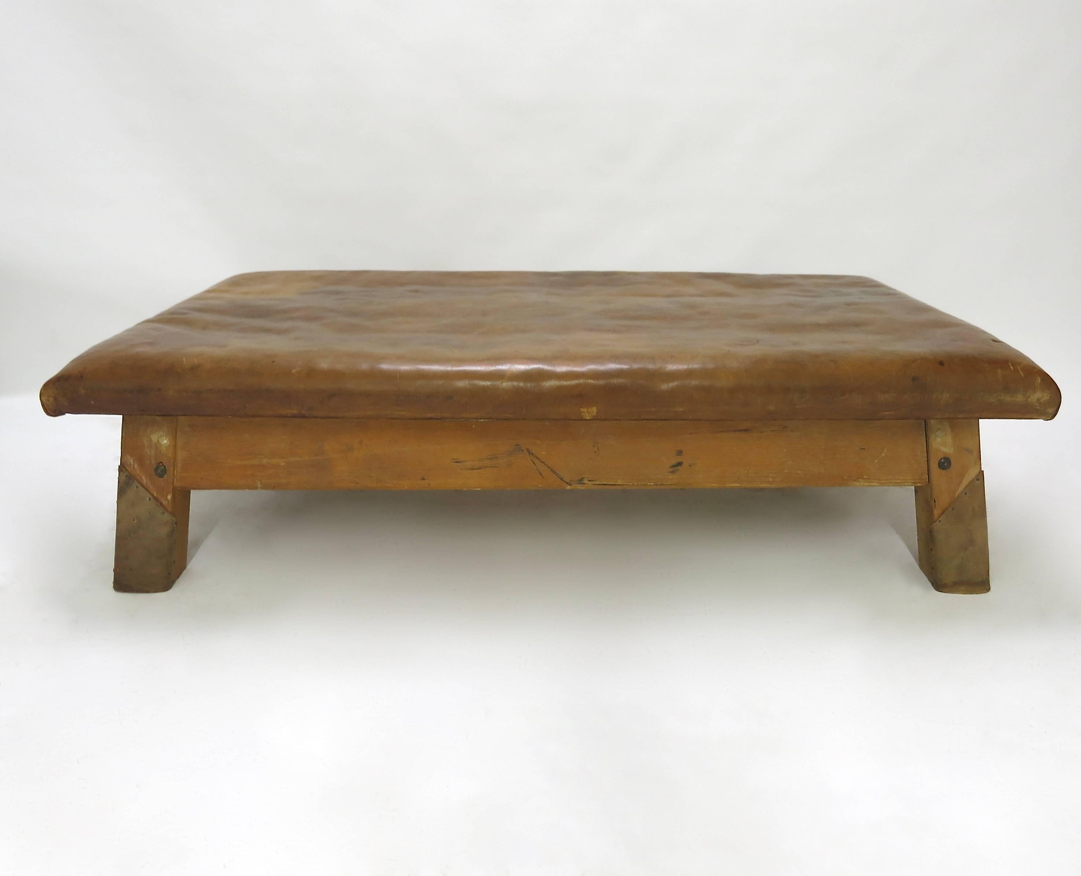 Strong, vintage European gymnasium bench with a removable leather covered top that sits in to the bench's solid wooden frame. The gym bench frame maintains its original markings where the straps and rings were once held. Each of the four legs has a