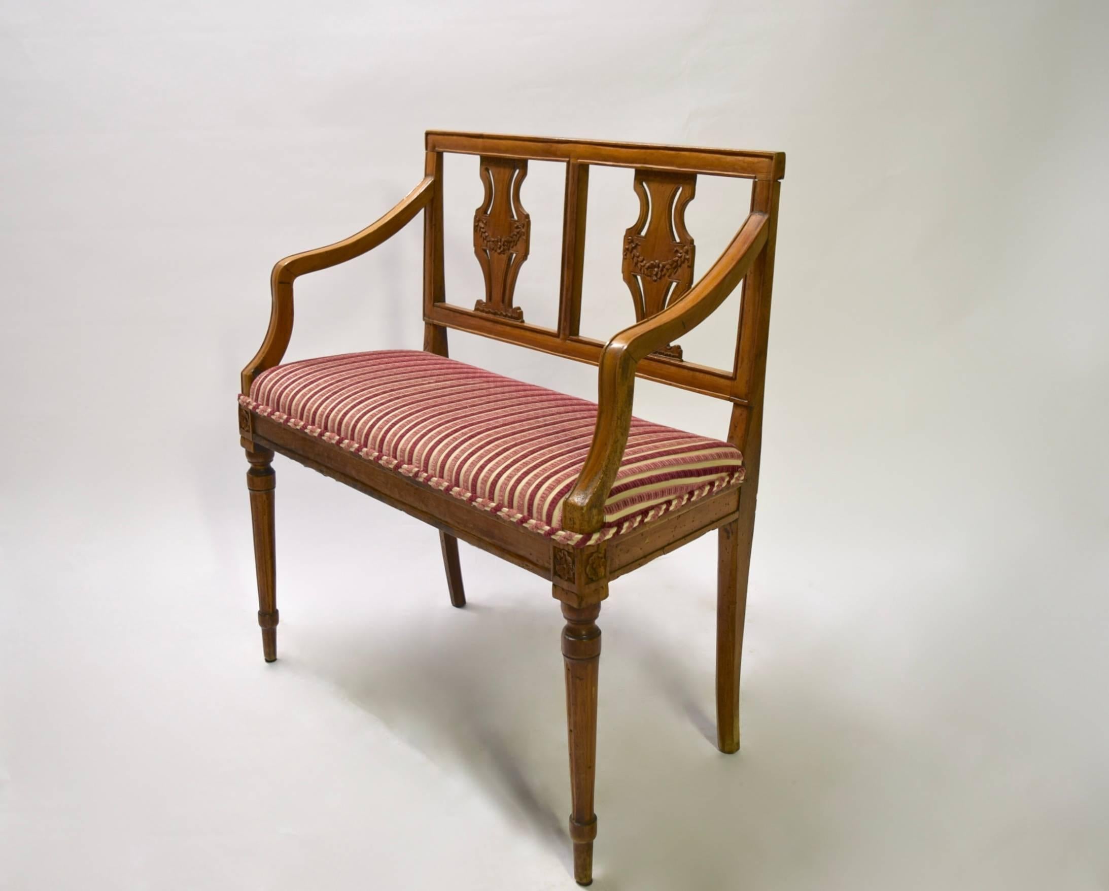 Settee has a mahogany frame with tapered hand front legs with hand-carved decorative flowers on each leg and the seat back. The cushion is upholstered in a modern striped fabric.