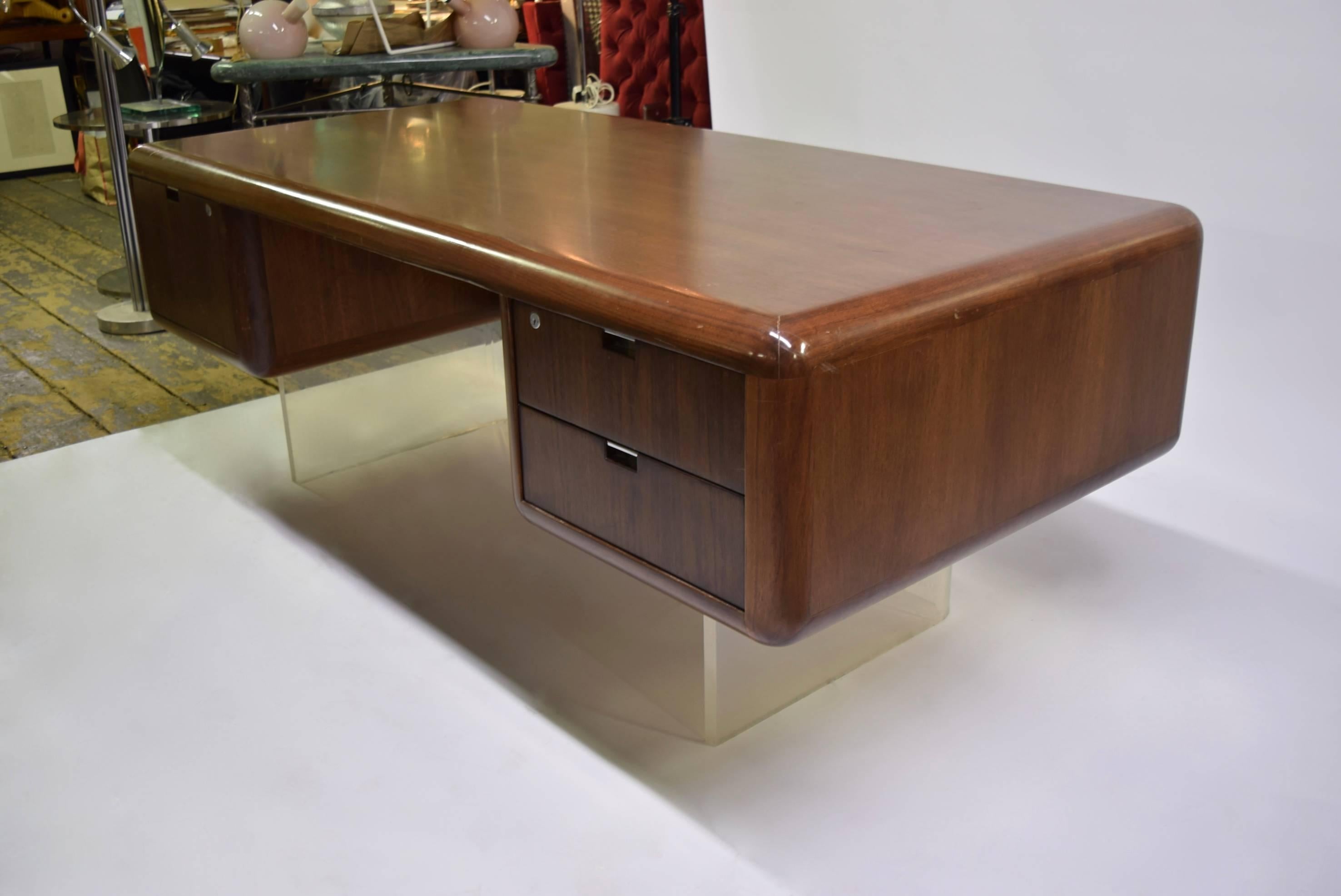 A floating desk in solid walnut with smooth round edges supported by a clear Lucite base designed in the 1960s by Vladimir Kagan.