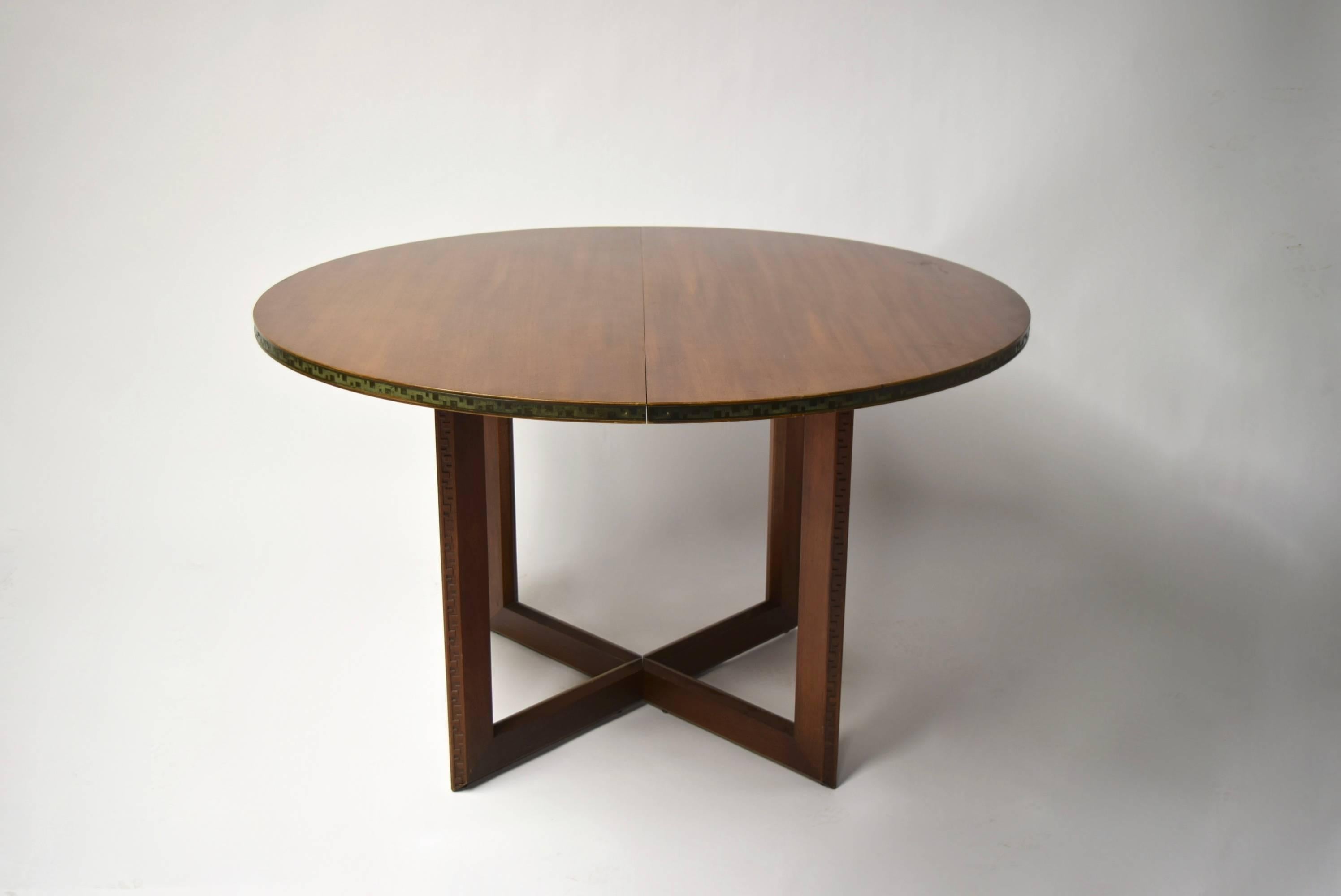 Round Taliesin mahogany dining table with an embossed copper banding, original patina preserved, along the top's border and the Taliesin design engraving along the edge of each leg. The table expands to an oval and each 16