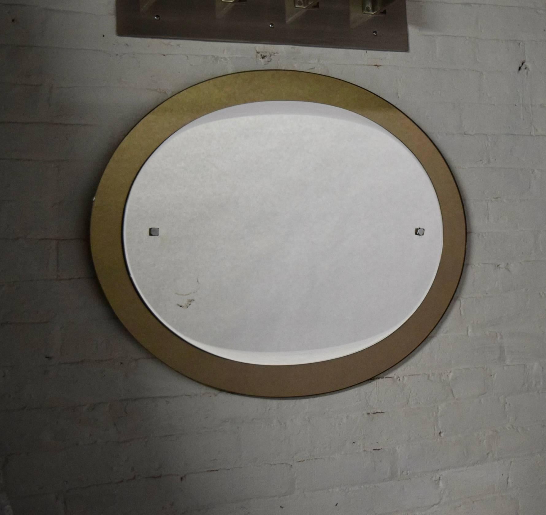 Wall-mounted, oval Italian mirror comprises a centre mirror with a tapering and curved bevel on the top and bottom, framed by a bronze toned smoked mirror and two square metal details. Silver age mark on one side, shown in image number 5.