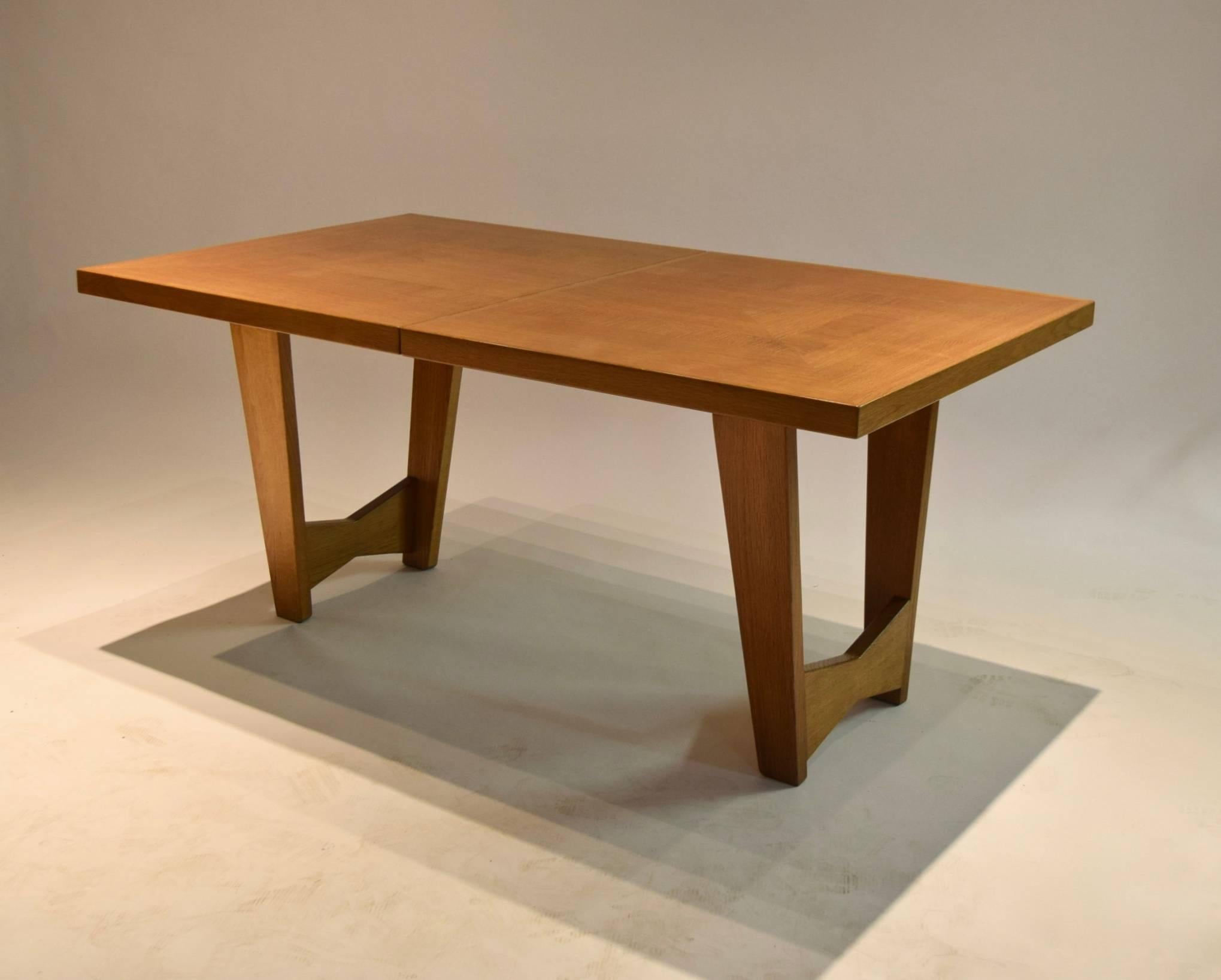 Extending dining table designed by Maurice Pré in oak wood, exhibiting very nice graining throughout. Comprises two 35 cm wide concealed leaves (approximately 13.75 inches wide) that are stored below the top's center opening, and two tapering leg