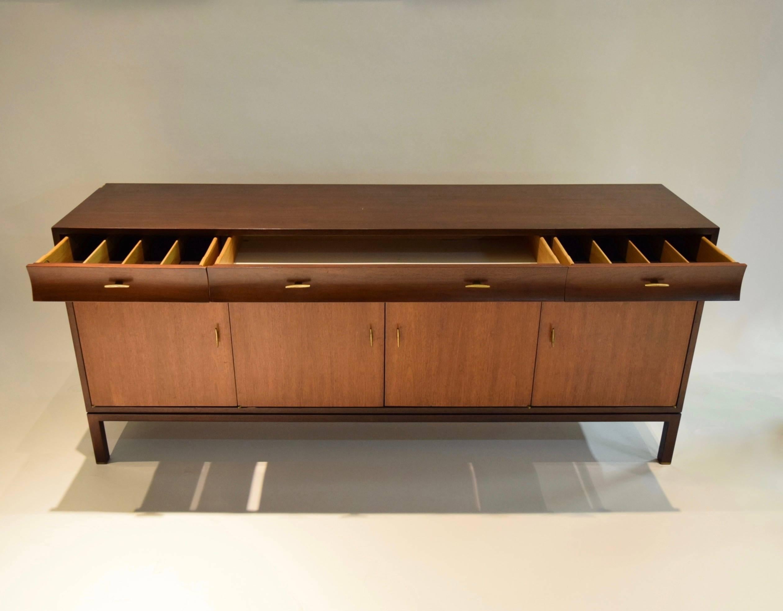 Sturdy and handsome buffet in very good, original condition by Edward Wormley for Dunbar in walnut wood with brass wishbone pulls and original labels.
There are four doors on the lower portion of the credenza and three concaving/ curved drawers in