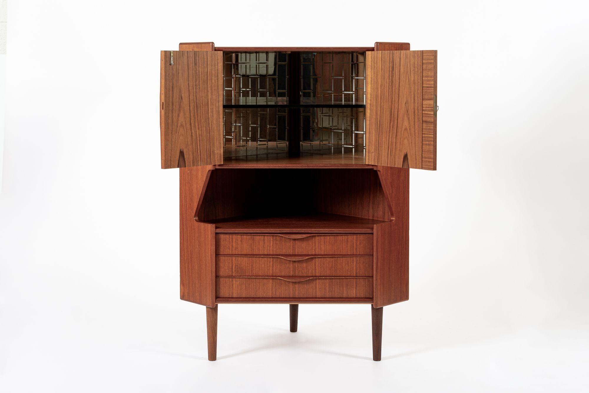 Questo grazioso mobile bar angolare in teak danese della metà del secolo scorso, realizzato da Gunni Omann per Omann Jun (attr.), è stato prodotto in Danimarca nel 1960 circa. Il classico design scandinavo ha linee pulite ed eleganti ed è ben