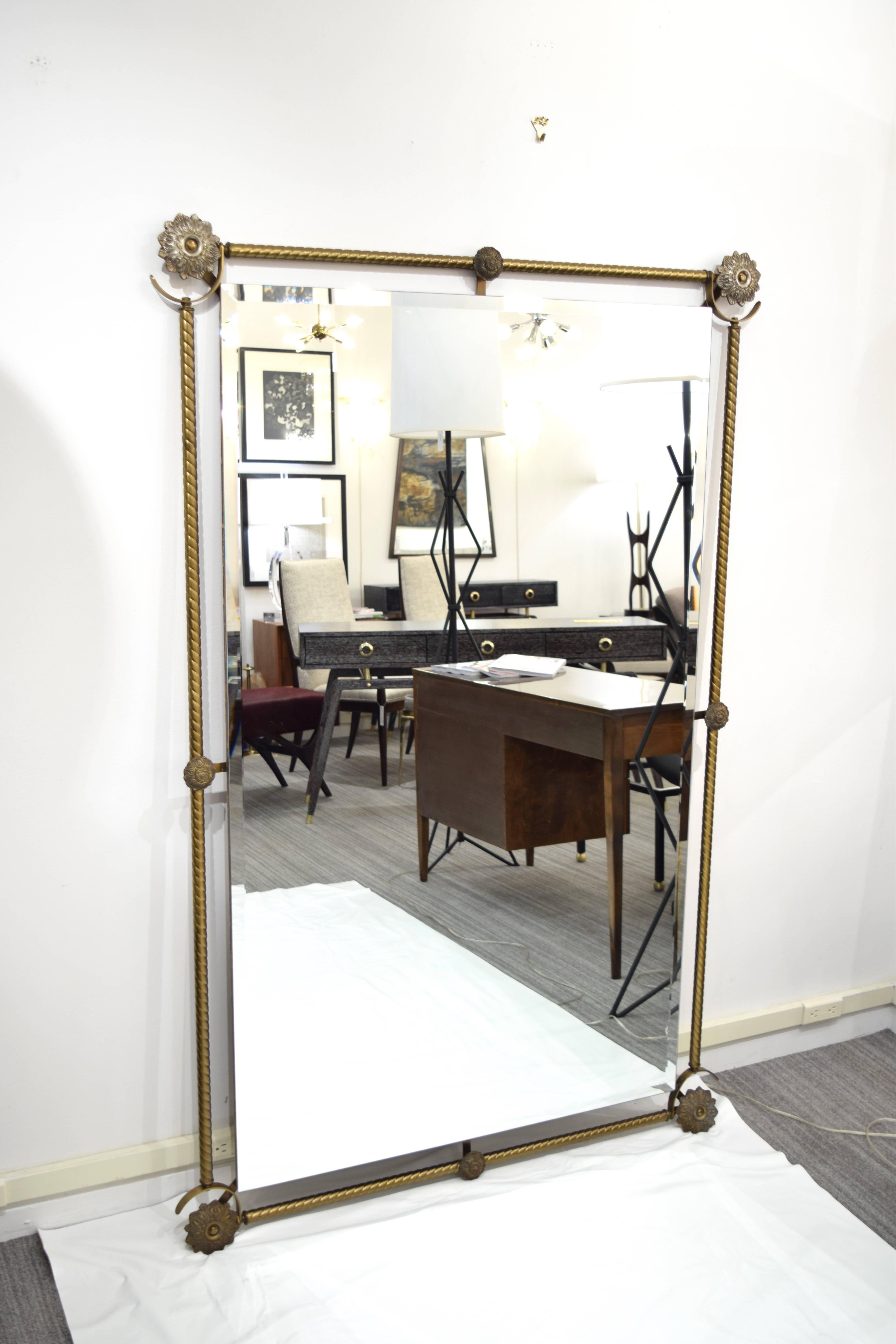 An extra large full length brass mirror with beveled interior mirror in the manner of Tommi Parzinger.  The mirror has a rope detail around the perimeter and large cast rosettes in the corners.  