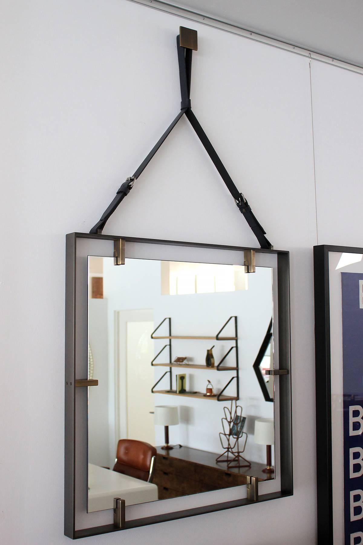 Large scale and expertly crafted design of a floating mirror with iron frame and thick brass detail.
Leather strap and brass buckle.
Brass square hanging puck.

Overall drop with Adjustable Strap: 57".