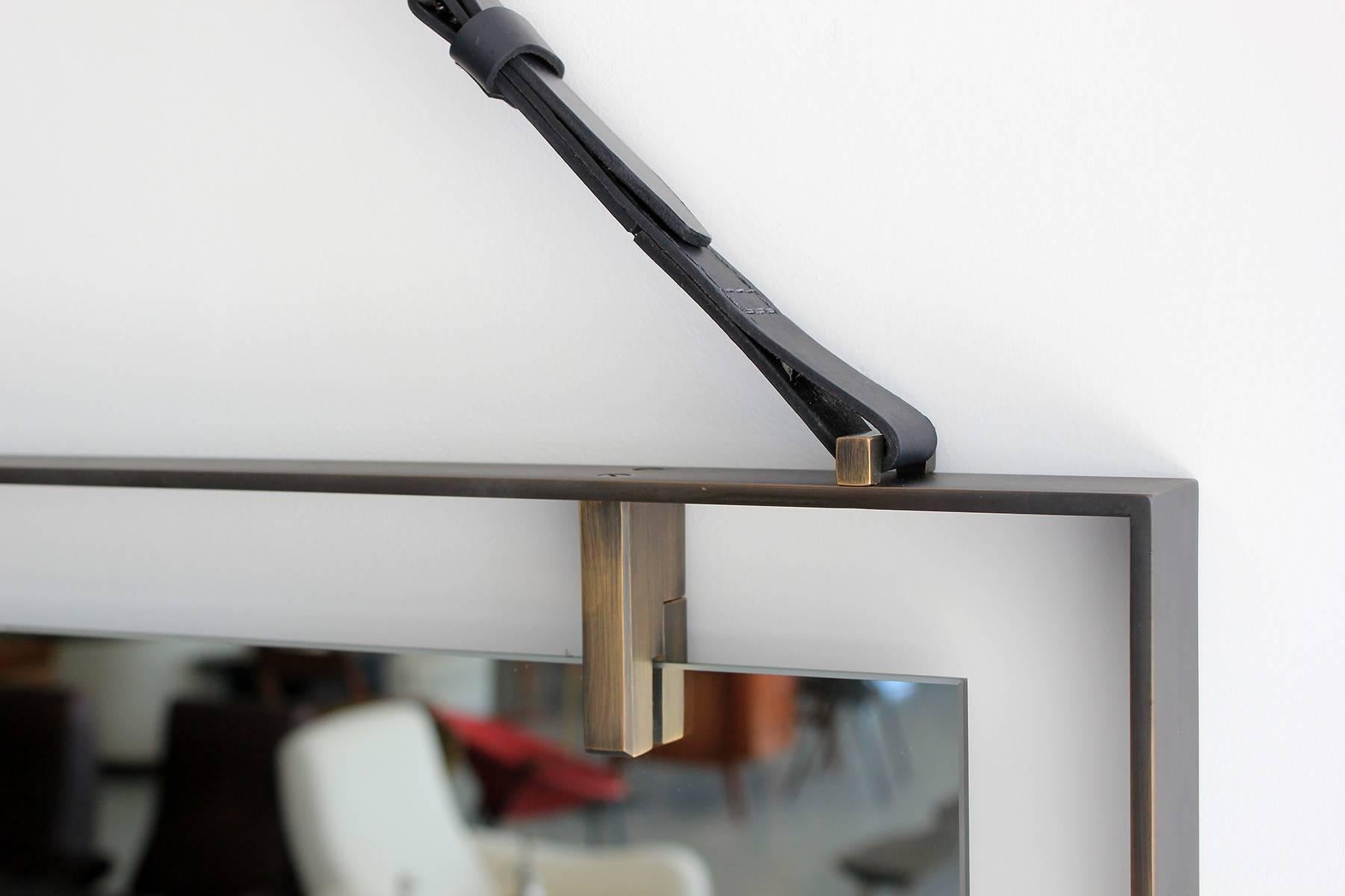 Specchio galleggiante di grandi dimensioni e sapientemente realizzato con cornice in ferro e dettagli in ottone. Cinturino in pelle e fibbia in ottone. Disco da appendere quadrato in ottone. Altezza complessiva con cinturino regolabile: 57