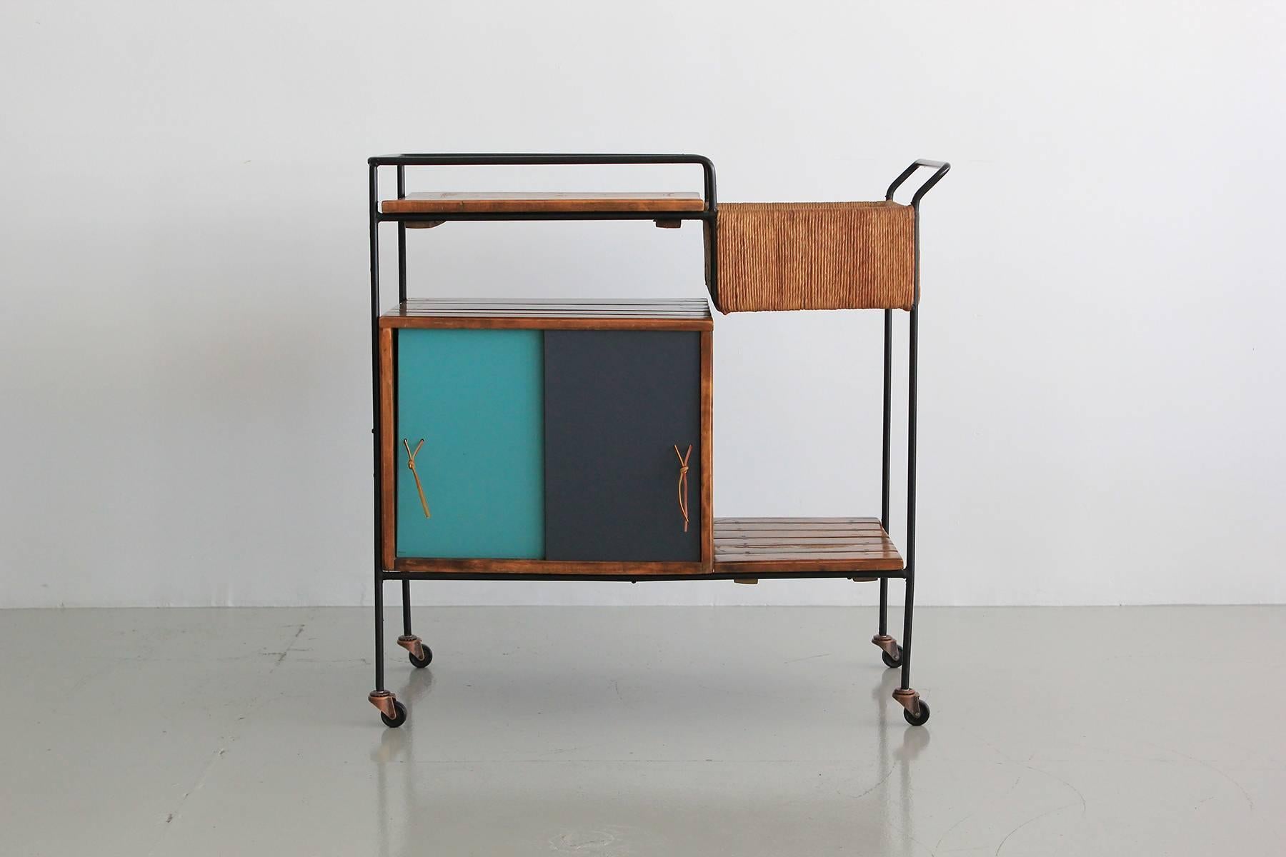 Great bar cart by Arthur Umanoff for Raymor. Black wrought iron frame, wood slat shelving, woven rushed storage compartment and sliding lacquered doors with extra storage.