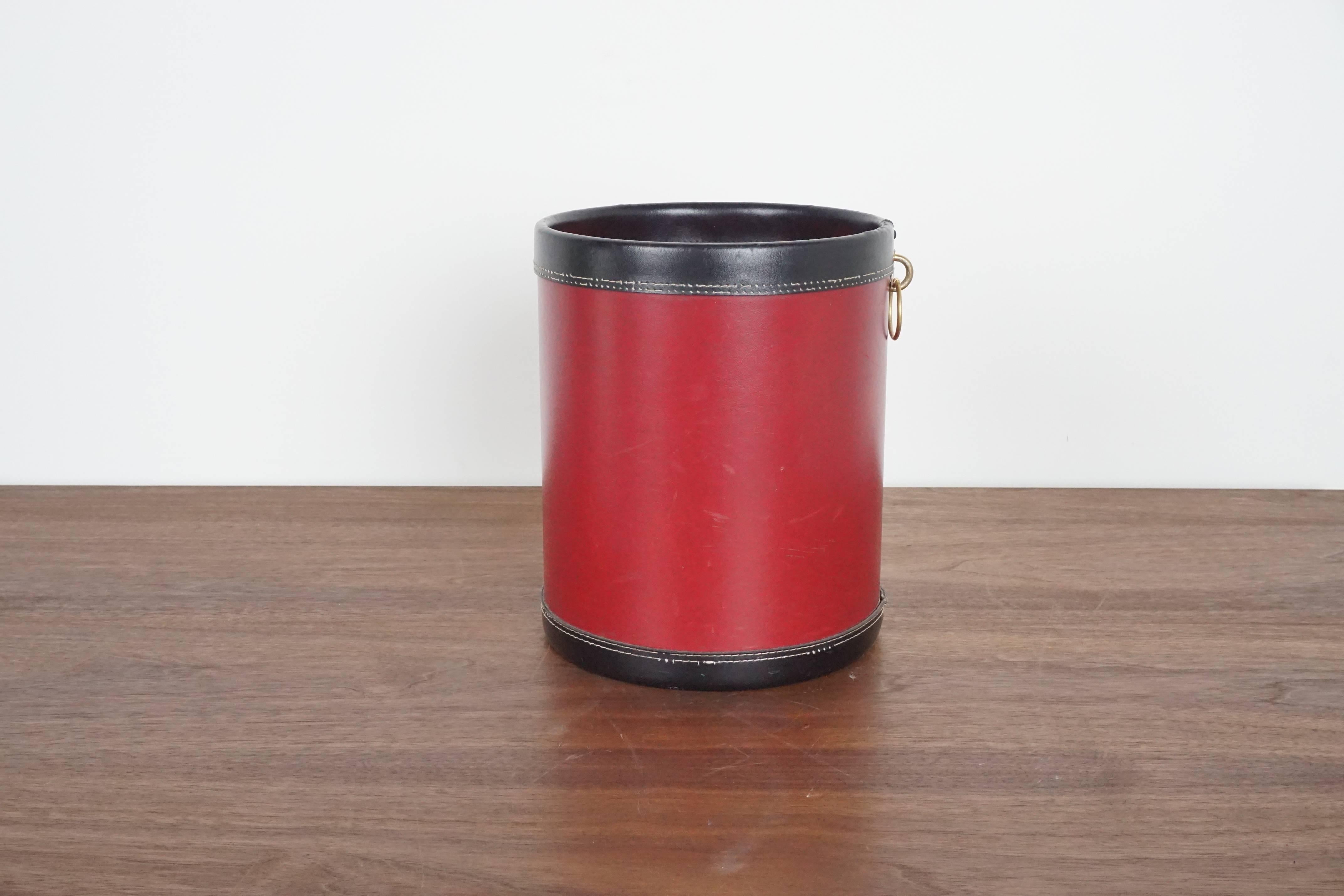 Red leather waste paper basket, France, 1950s in the style of Jacques Adnet. Black leather trim with contrast stitching and brass detailing.