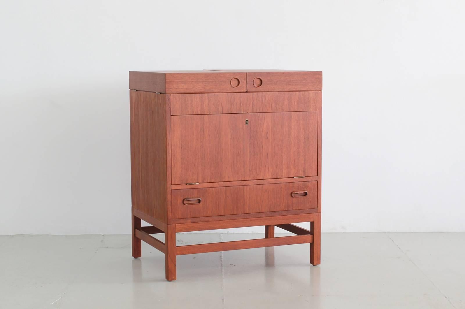 Great Danish designed teak bar with lift top that opens up to reveal storage space for bottles and counter space for glasses. Middle cabinet folds down to reveal extra storage and bottom drawer.
Wonderful unique design!

Dimensions when