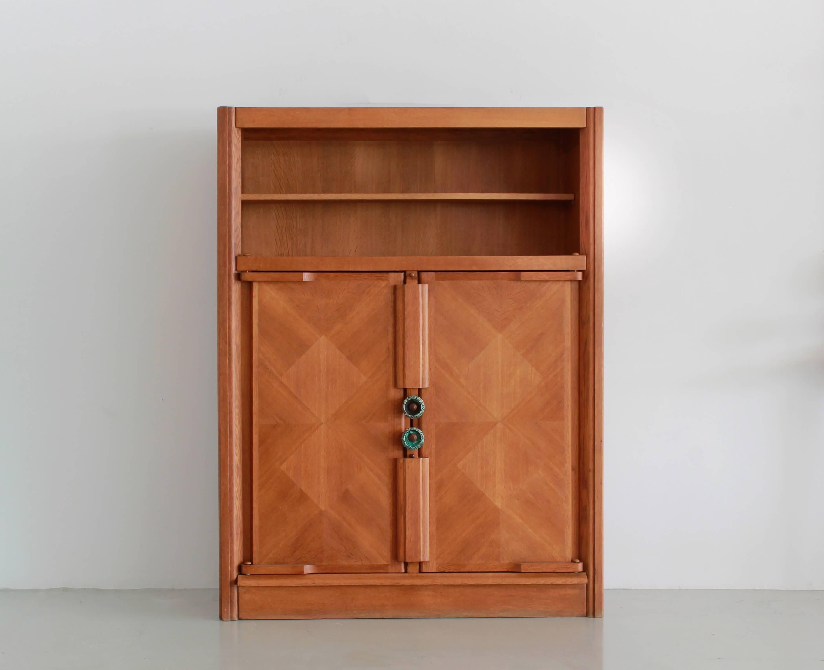 Incredible cabinet by Robert Guillerme (1913-1990) and Jacques Chambron (1914-2001) with an open display shelf and interior shelving enclosed by oak doors in geometric grain pattern and signature ceramic hardware. 
Gorgeous inlaid patterned wood.