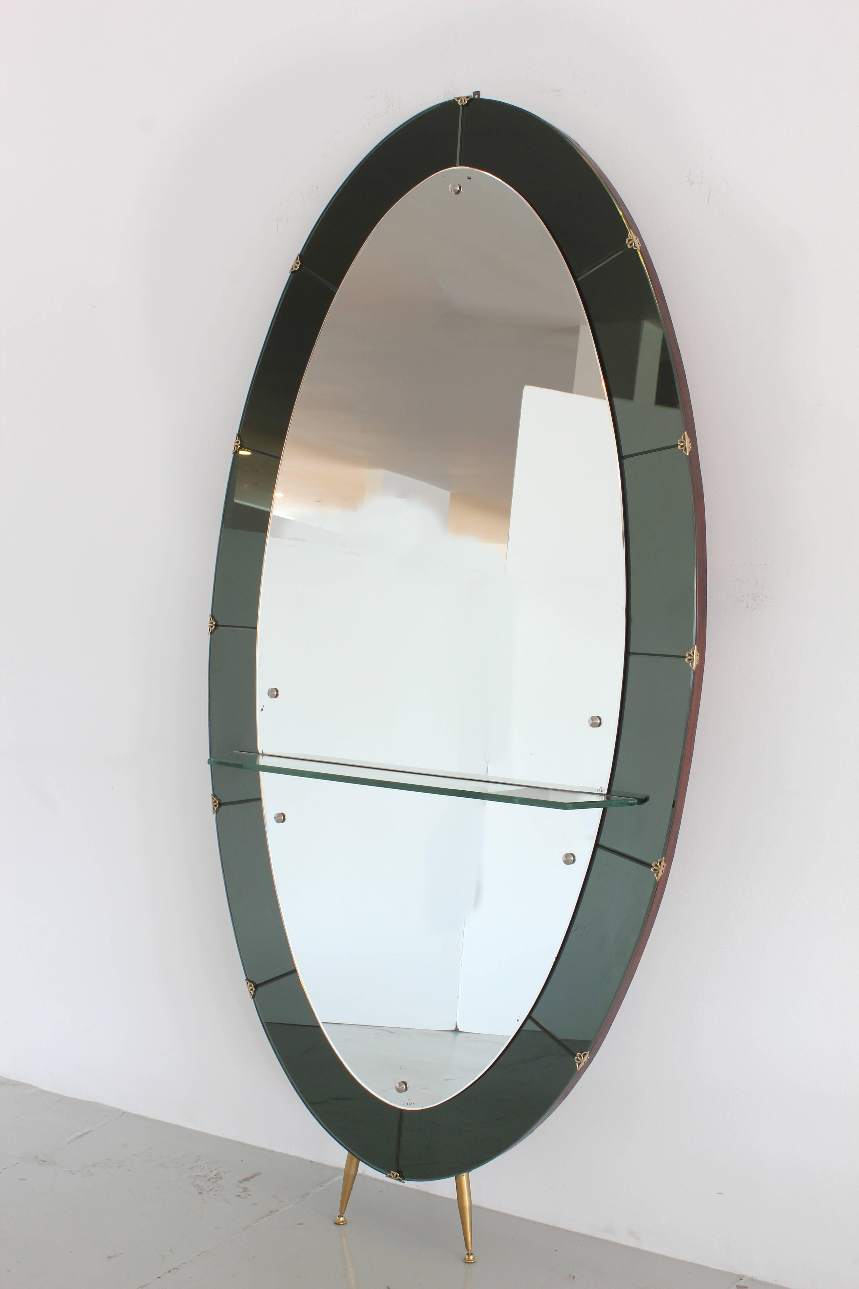 Incredible Italian mirror by Cristal Art featuring signature smoke tinted mirror frame with tapered brass feet and brass detailing. Glass shelf allows for display or vide-poche accessories.