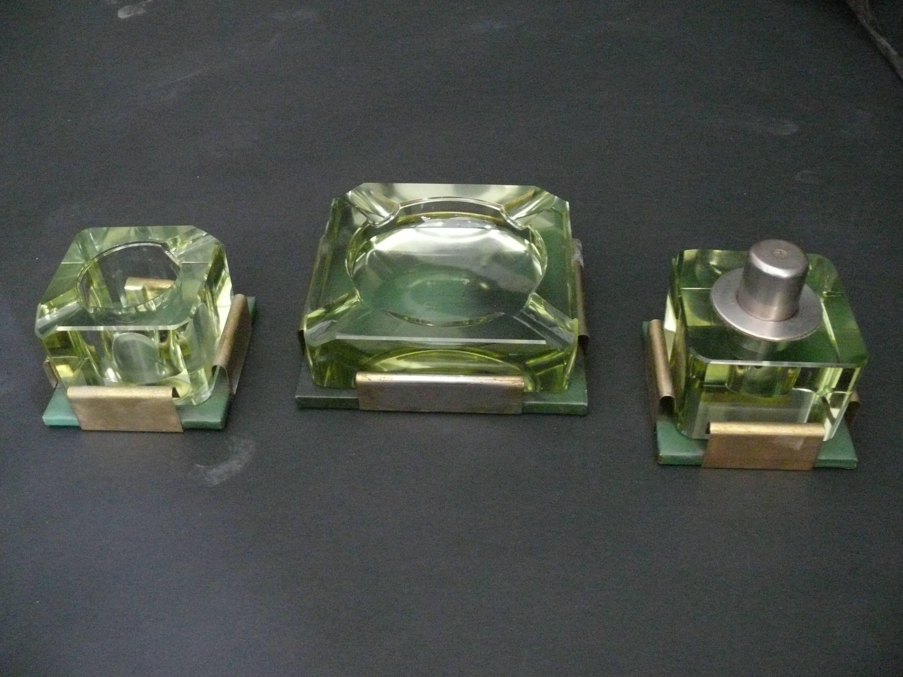 Exceptional vintage three-piece smoking set with vibrant green crystal glass. Each piece sits atop a green leather coaster adorned with gold-plated brass edges. Very unique.