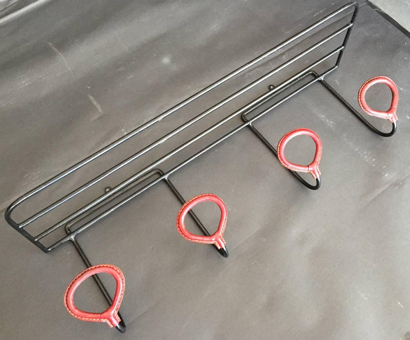 Spectacular coat rack by Jacques Adnet. Iron frame with top shelf and four hooks. Burgundy leather hooks with signature Adnet contrast stitching in excellent vintage condition.