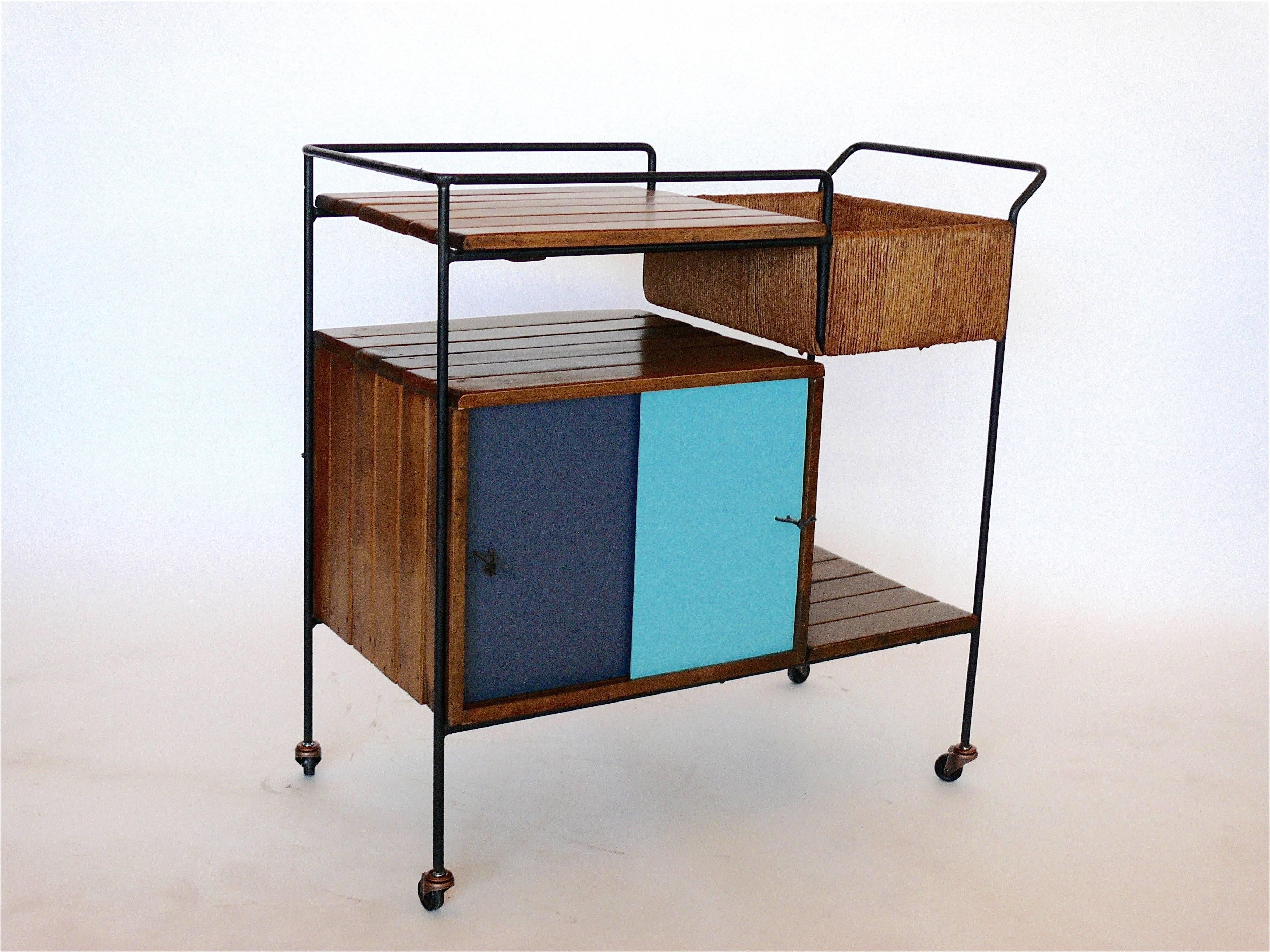 Fantastic bar cart by Arthur Umanoff for Raymor. Iron framed cart features slatted wood, multiple rushed wicker shelves and an enclosed cabinet with sliding doors that have been newly lacquered. 
Great colors and in excellent vintage condition.