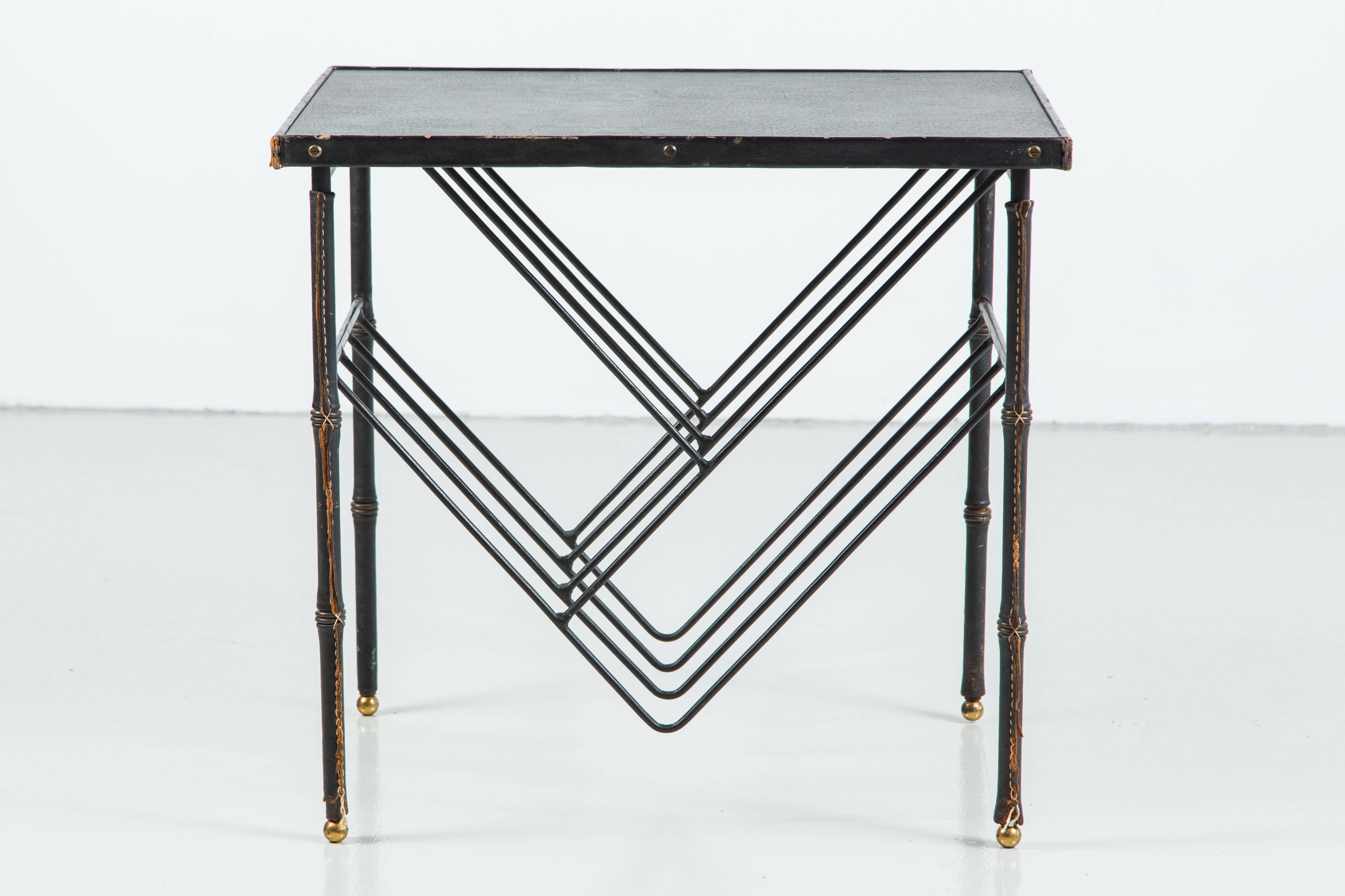 Jacques Adnet attributed side table with signature black leather and brass bamboo legs and skai leather top. Brass hardware detailing and angular iron wire bookshelf built-in to access from both sides. 
Brilliant design.